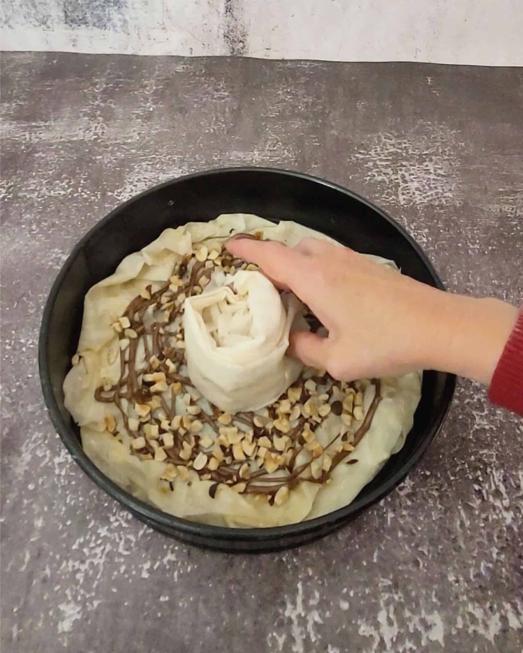 adding first piece of folded phyllo into cake pan