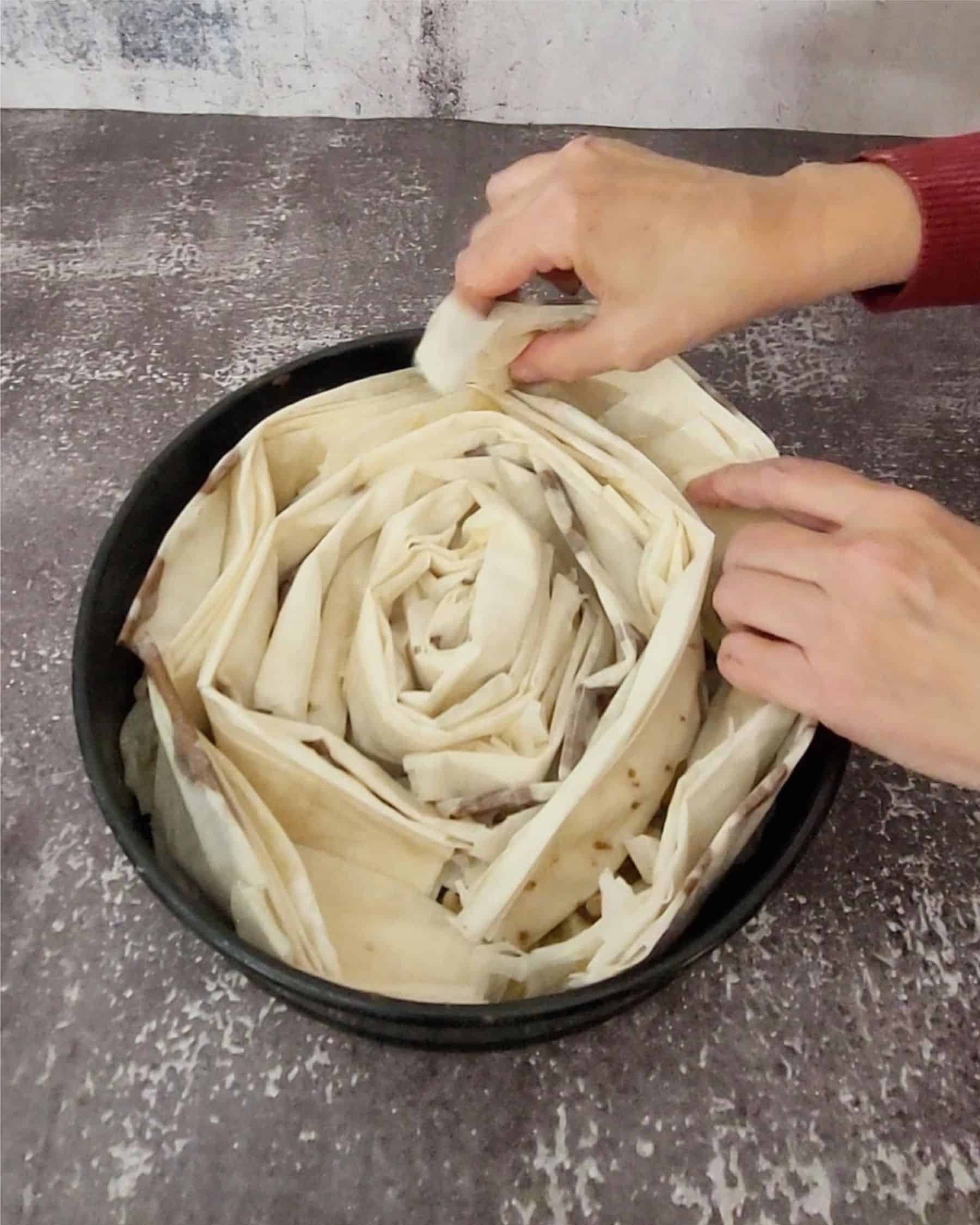 adding last piece of folded phyllo dough into springform cake pan