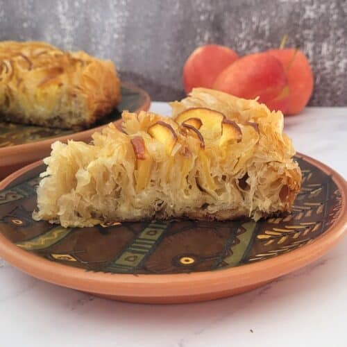 close up of a slice of crinkle cake with apples and remainder of cake in background