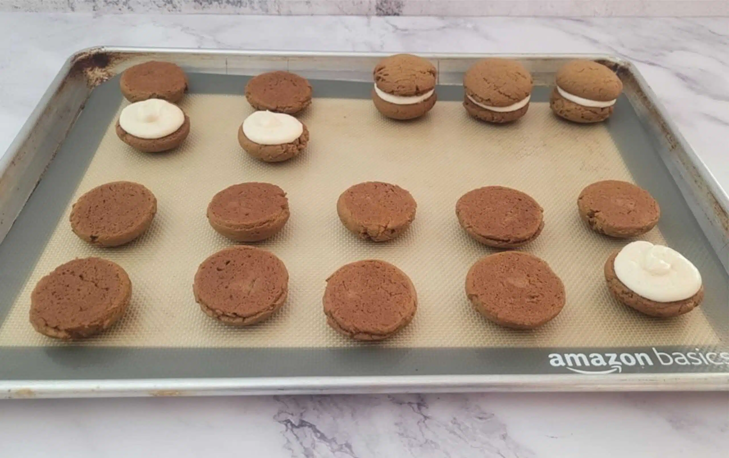 whoopie pies on a sheet pan being filled with cream cheese icing