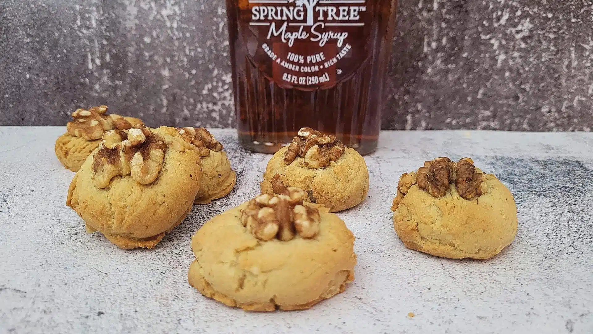 maple cookies with half a walnut piece on top and a bottle of maple syrup in the background