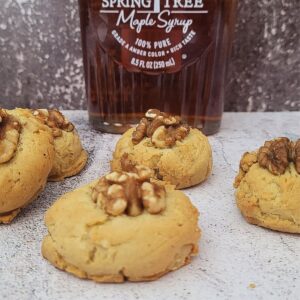 maple walnut cookies on a countertop with a bottle of maple syrup in the background