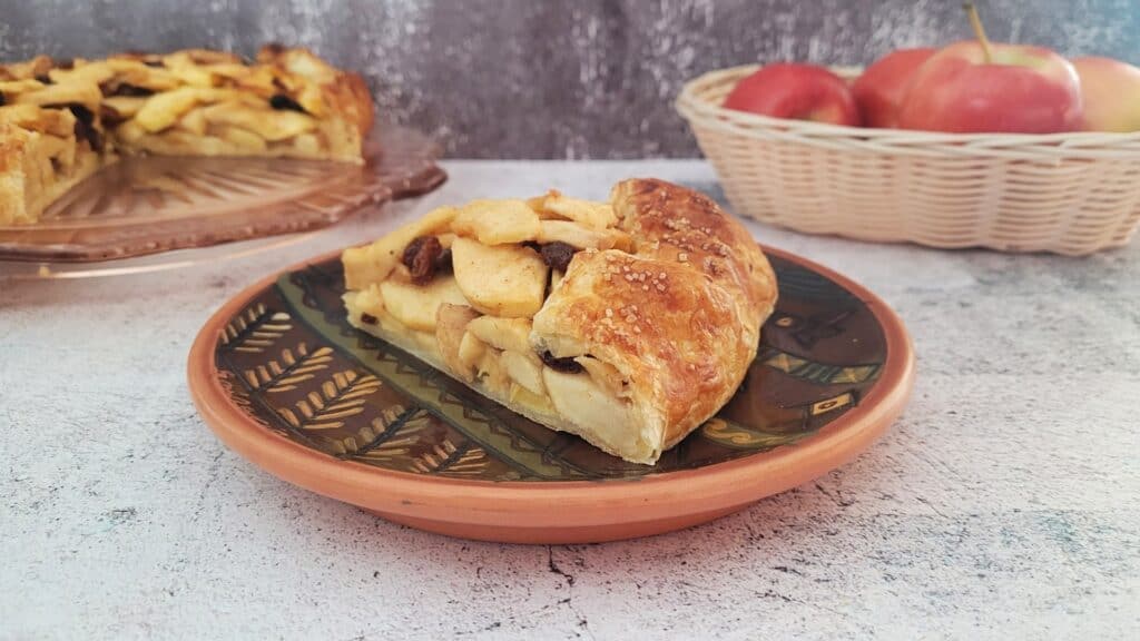 slice of apple galette on a plate with remainder of dessert in the background