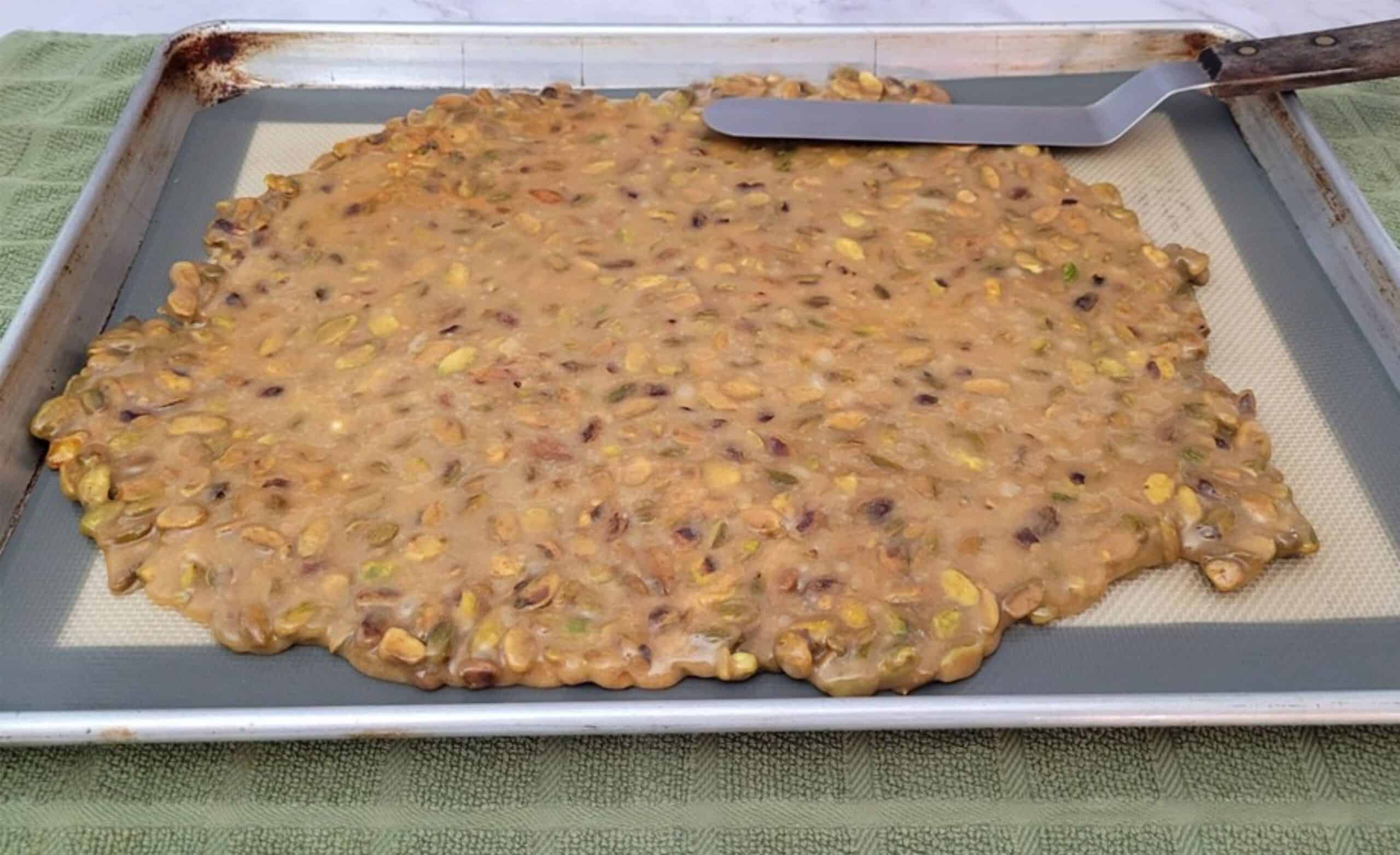 spreading hot caramel with pistachios on a sheet pan