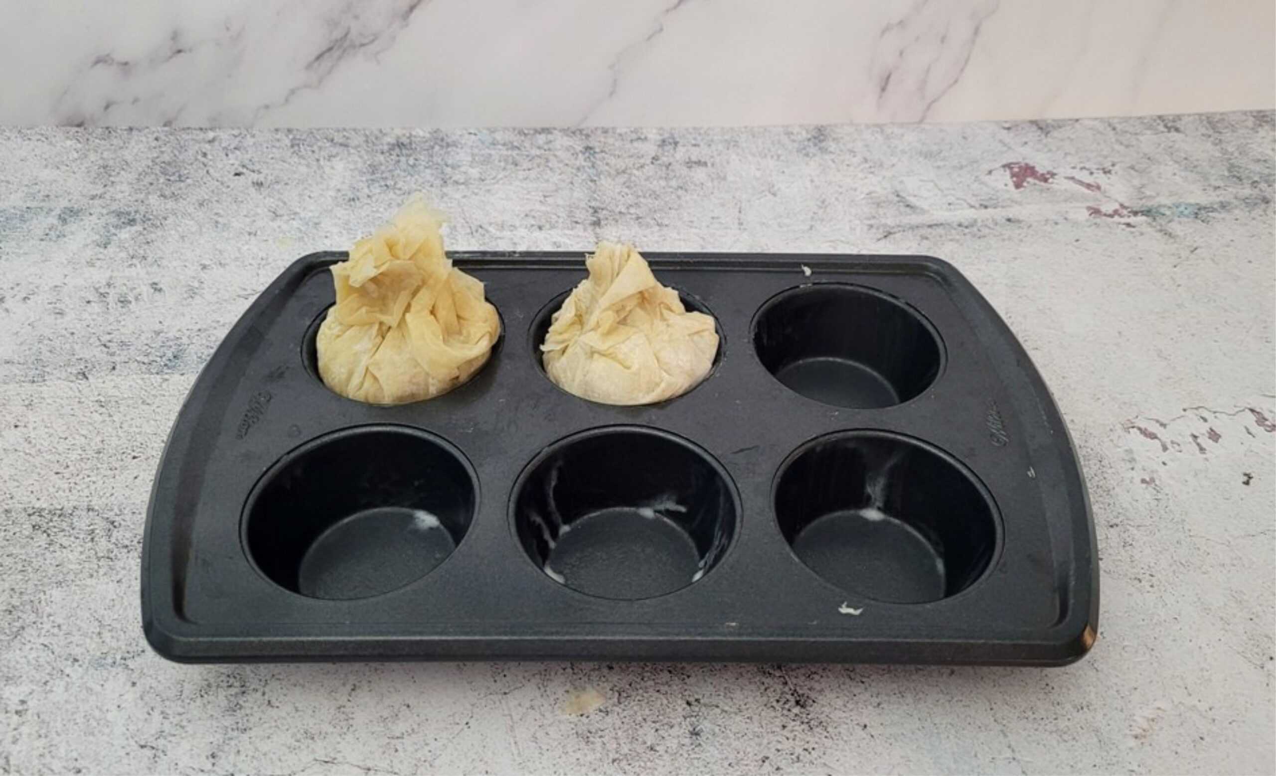 two baklavas in a muffin pan with the phyllo dough on top scrunched together to seal the dessert