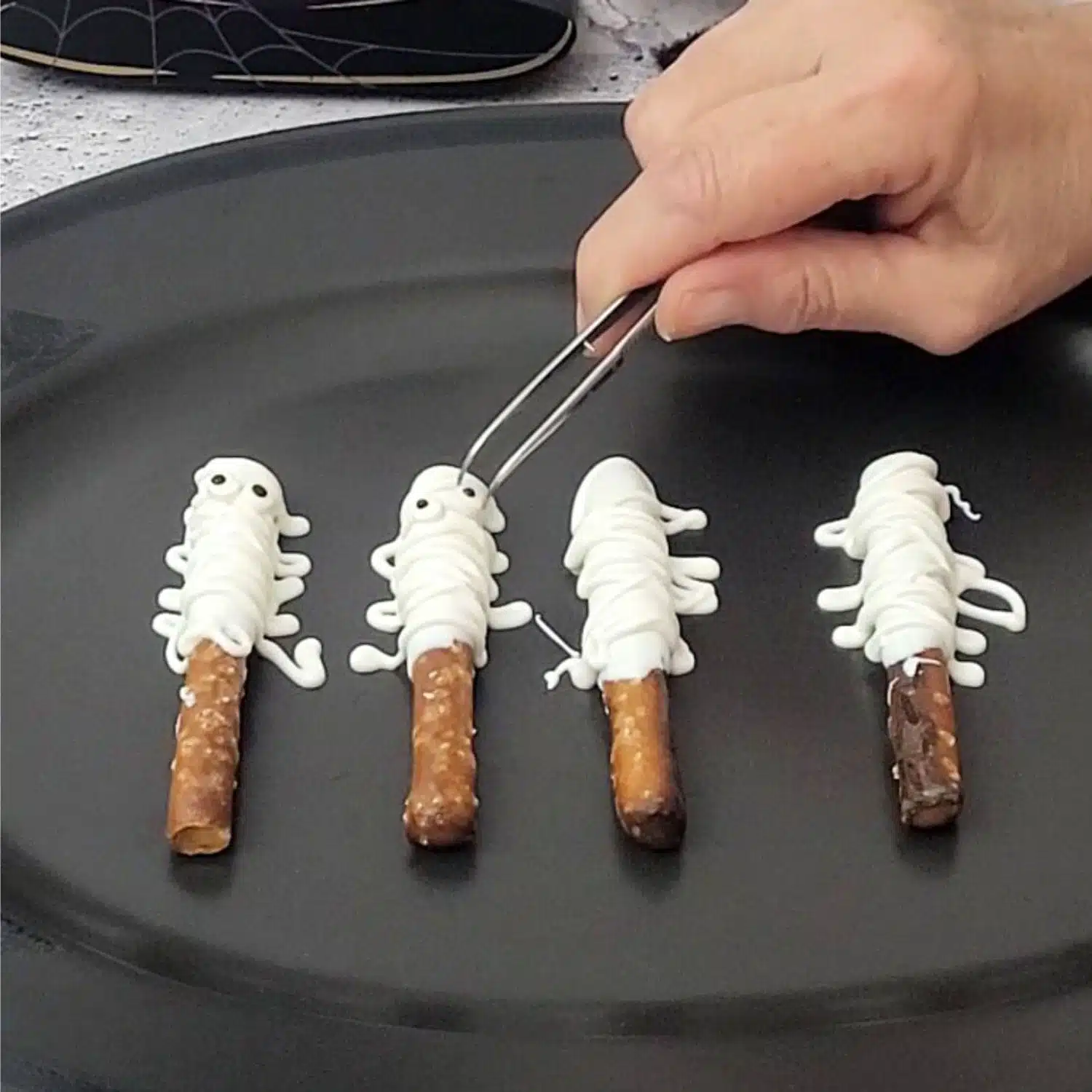 using a tweezers to place googly eyes on Halloween mummy pretzels