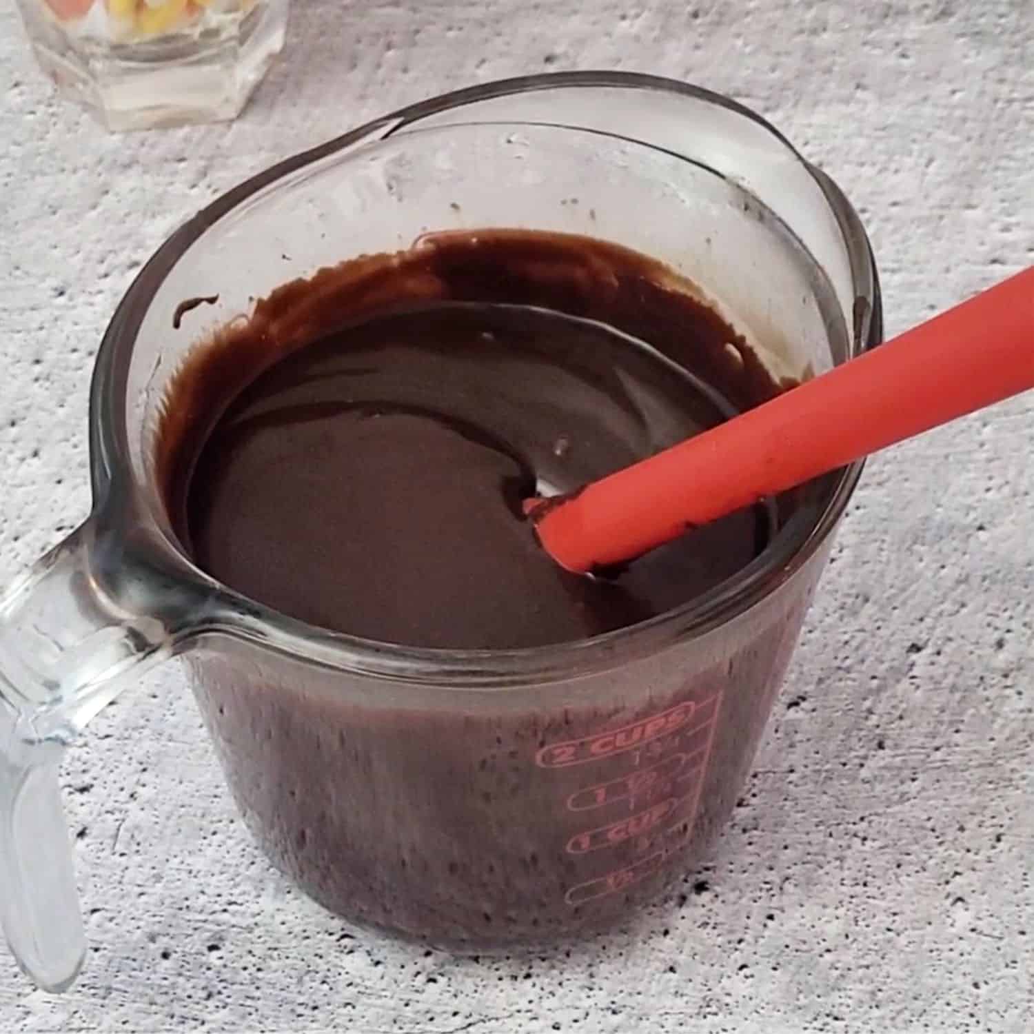 chocolate topping in a glass cup to pour over Halloween Candy Corn Brownies