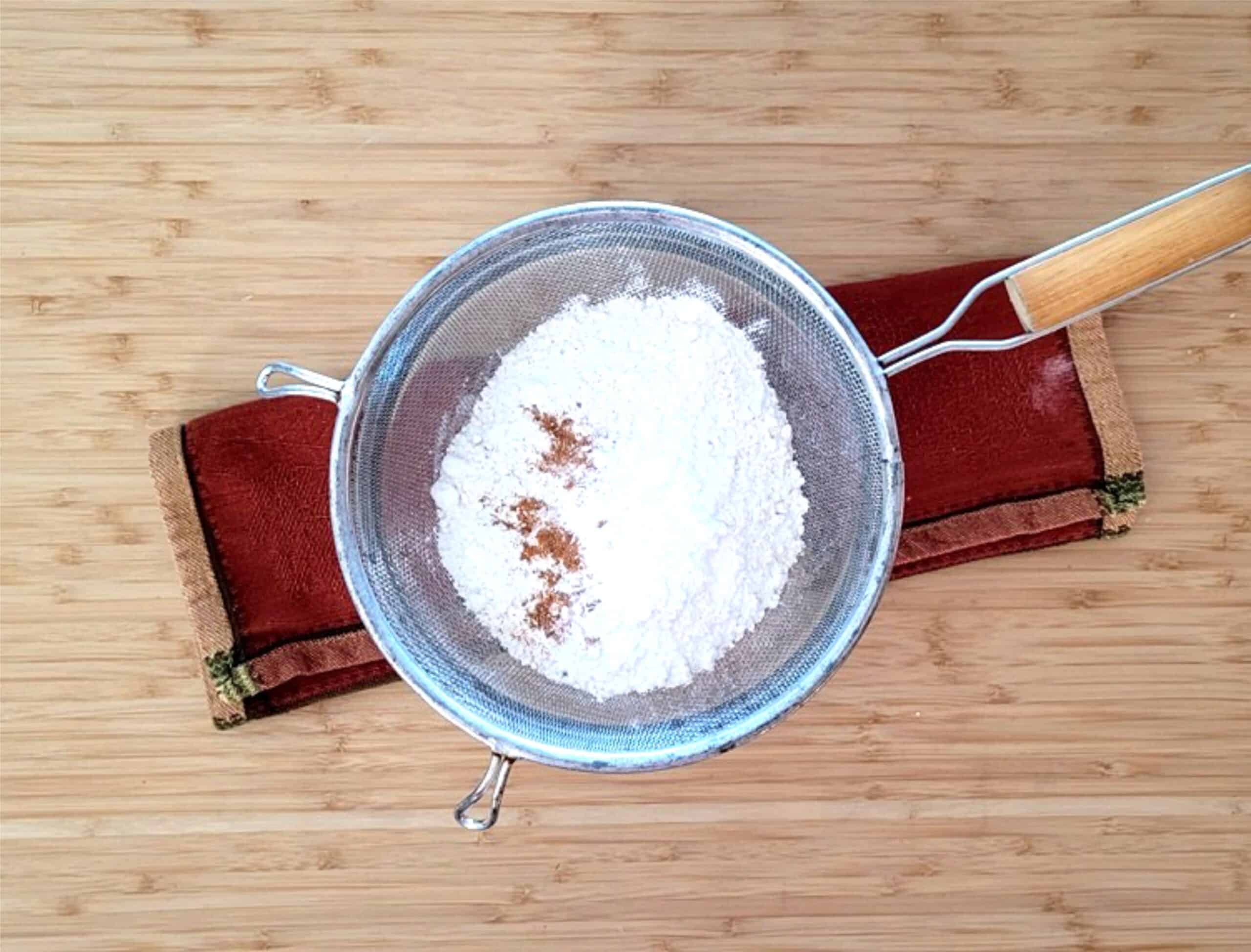 dry ingredients in a sieve including flour, cinnamon, baking powder and baking soda