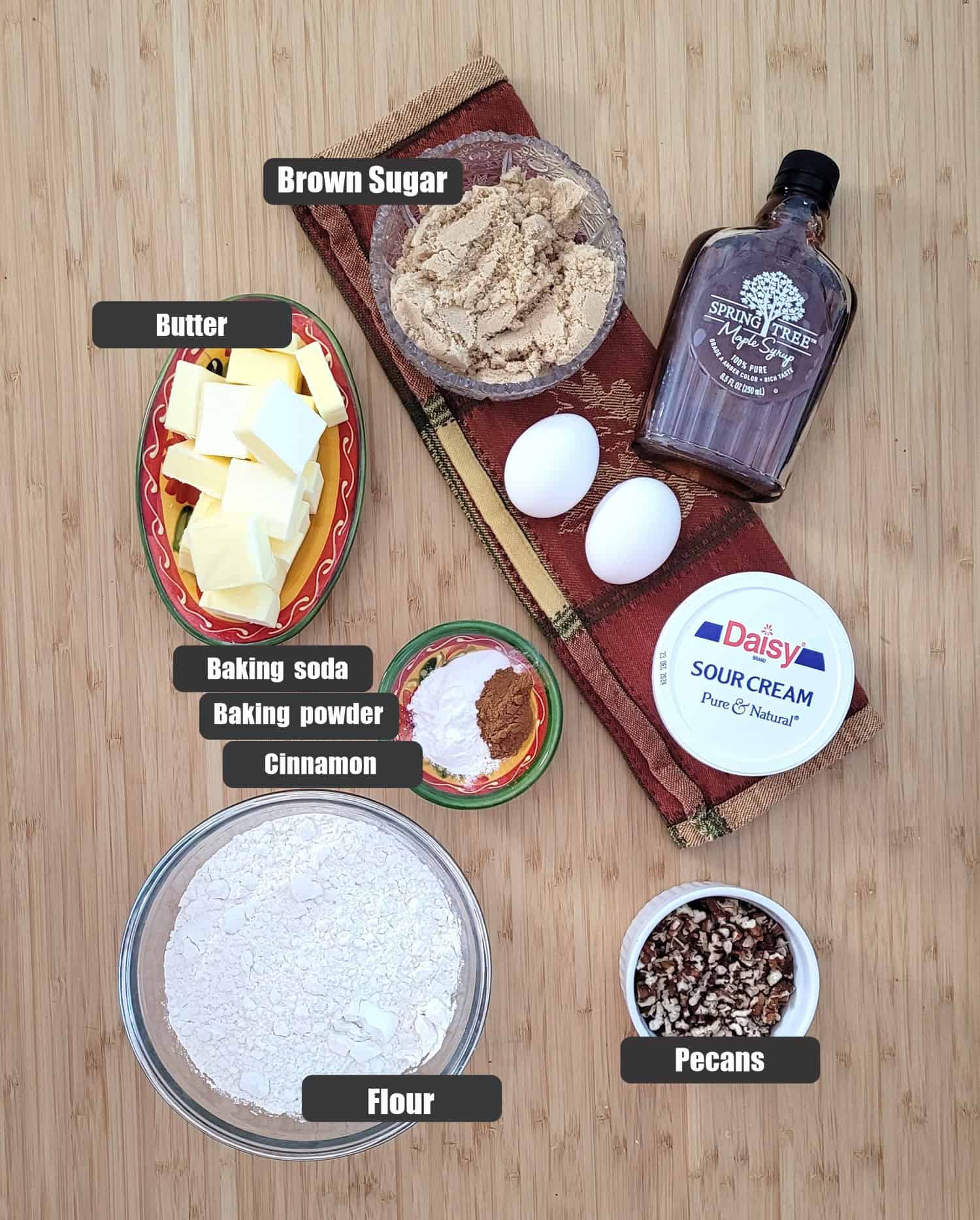 ingredients needed for maple cake including flour, pecans, baking powder, baking soda, cinnamon, sour cream, brown sugar and maple syrup