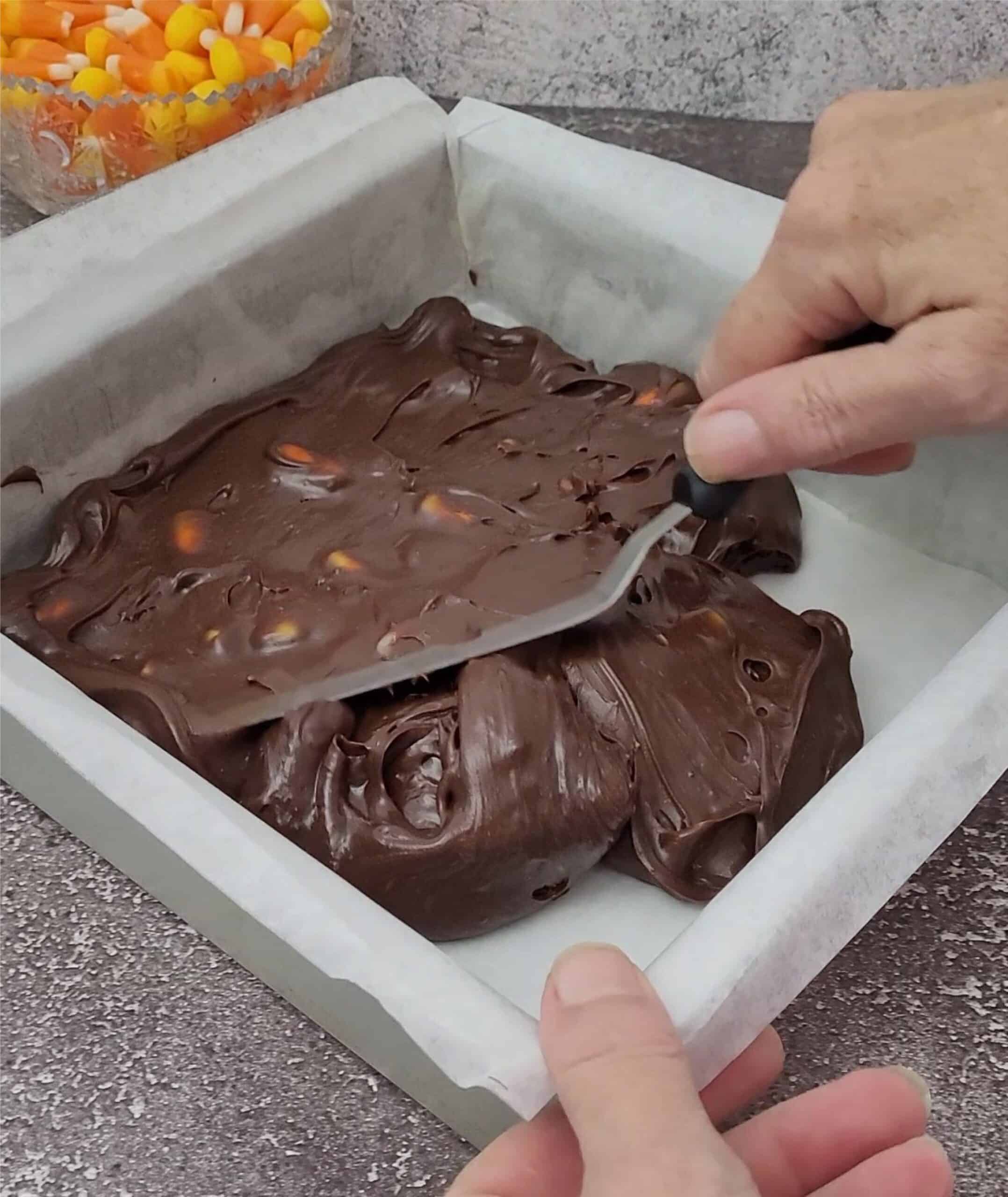 spreading chocolate fudge with candy corn pieces into a square pan