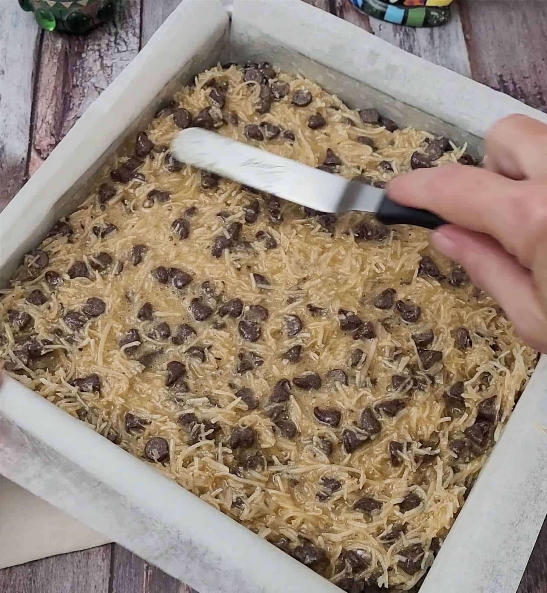 spreading coconut and chocolate topping over shortbread cookie bar base using an offset spatula