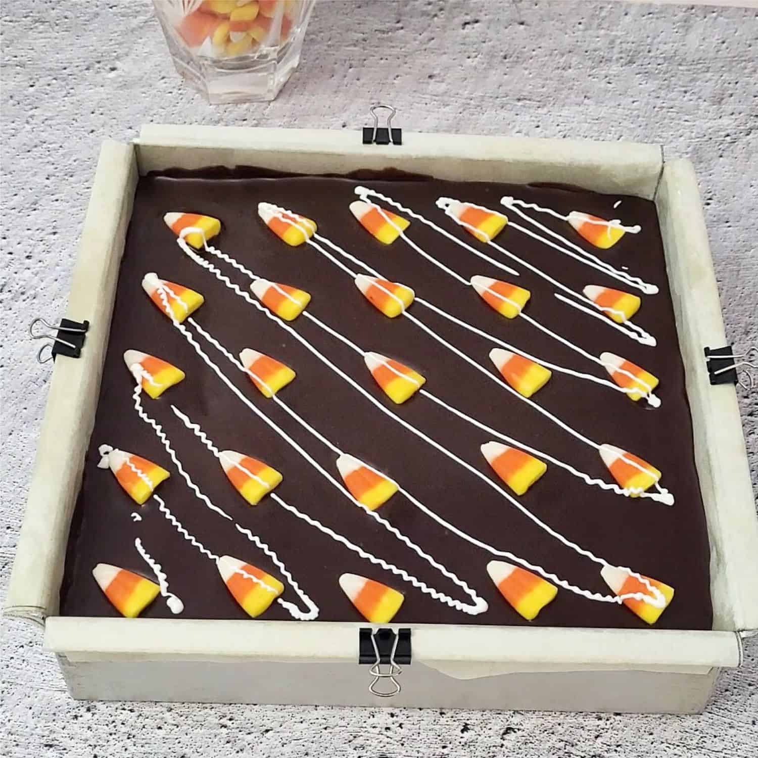 brownies in pan with fudge topping, candy corn and white chocolate drizzle on top