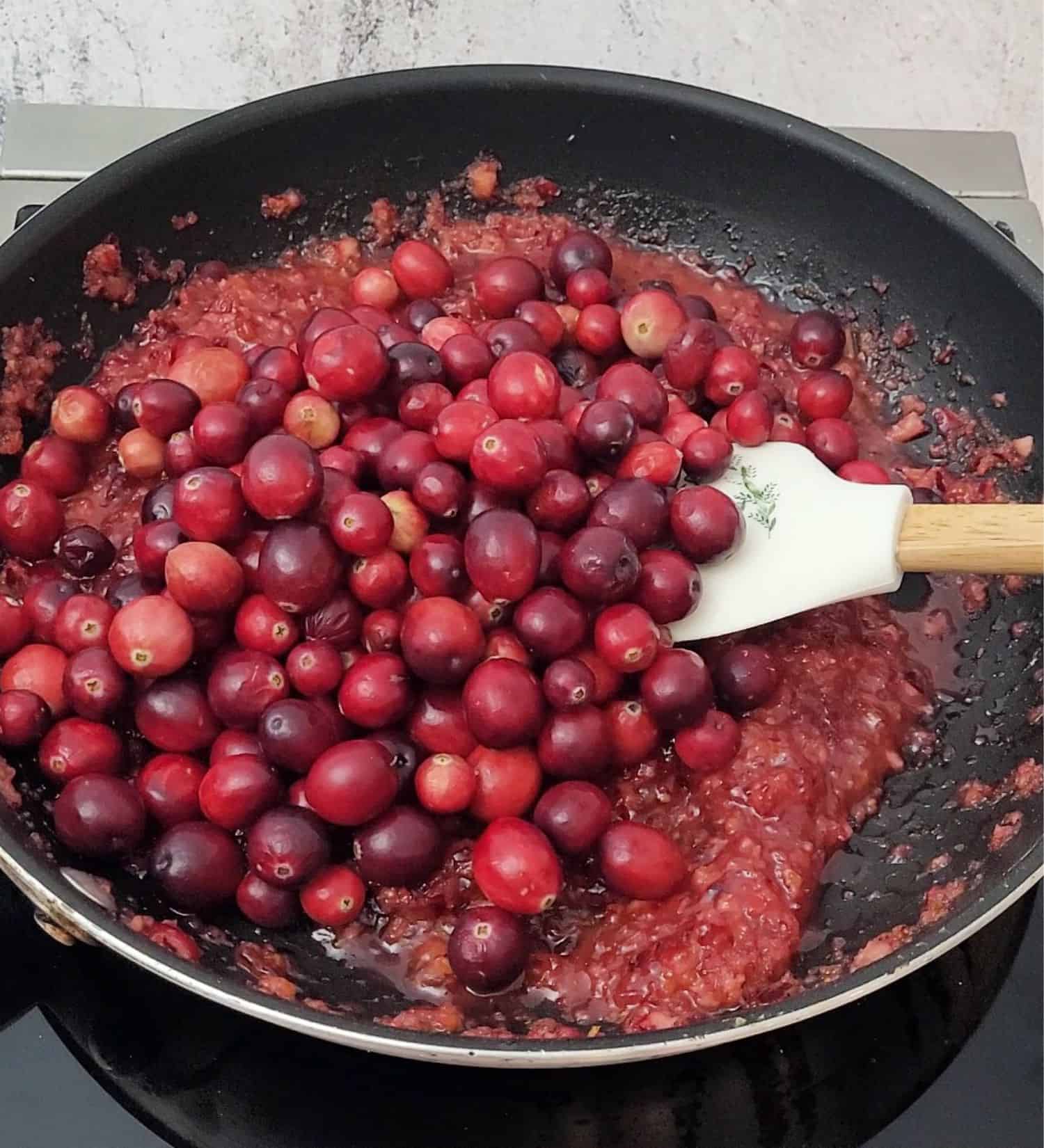 stirring cranberries in saucepan with cranberry and orange slurry