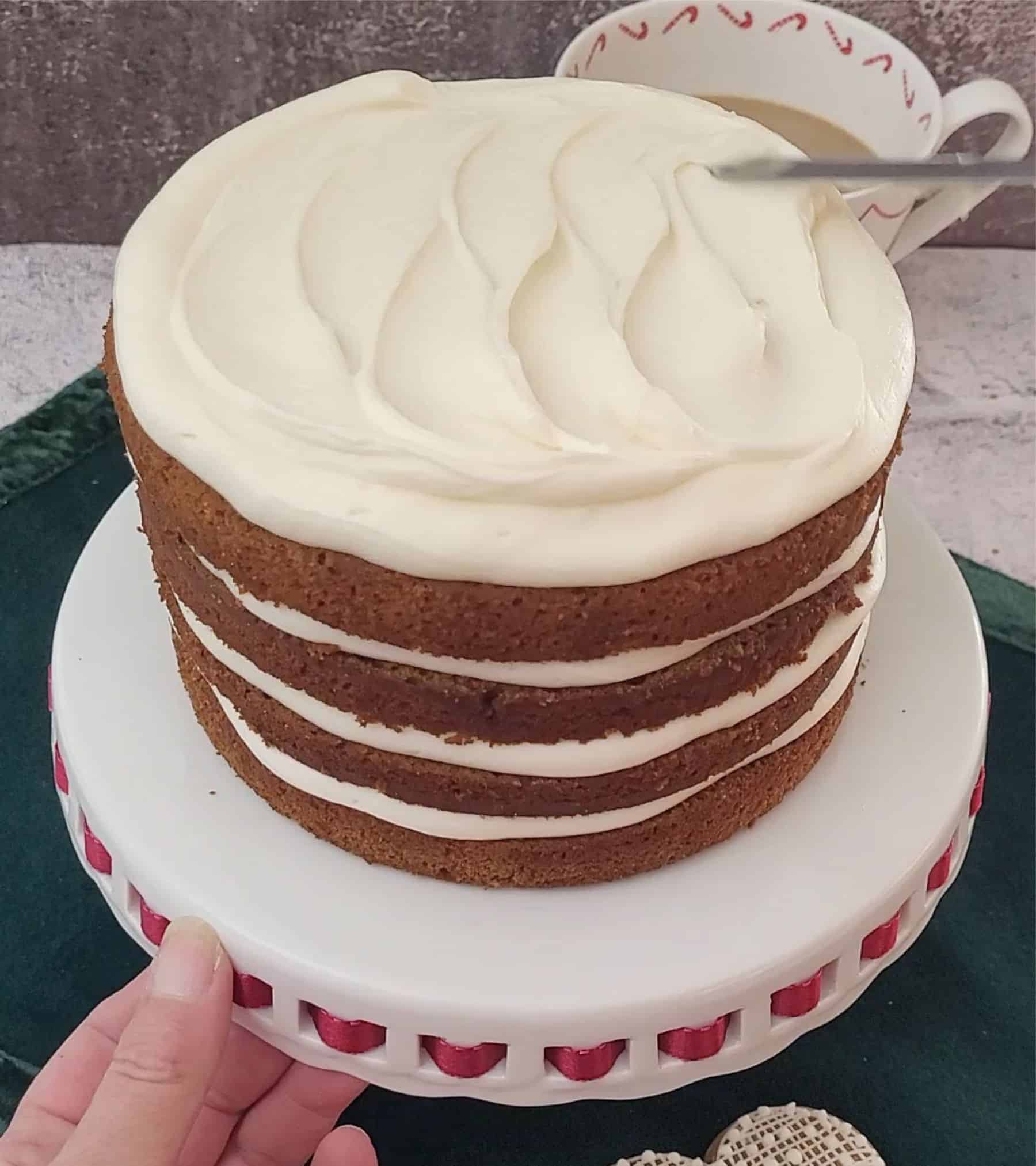 adding top layer of cream cheese frosting to gingerbread cake