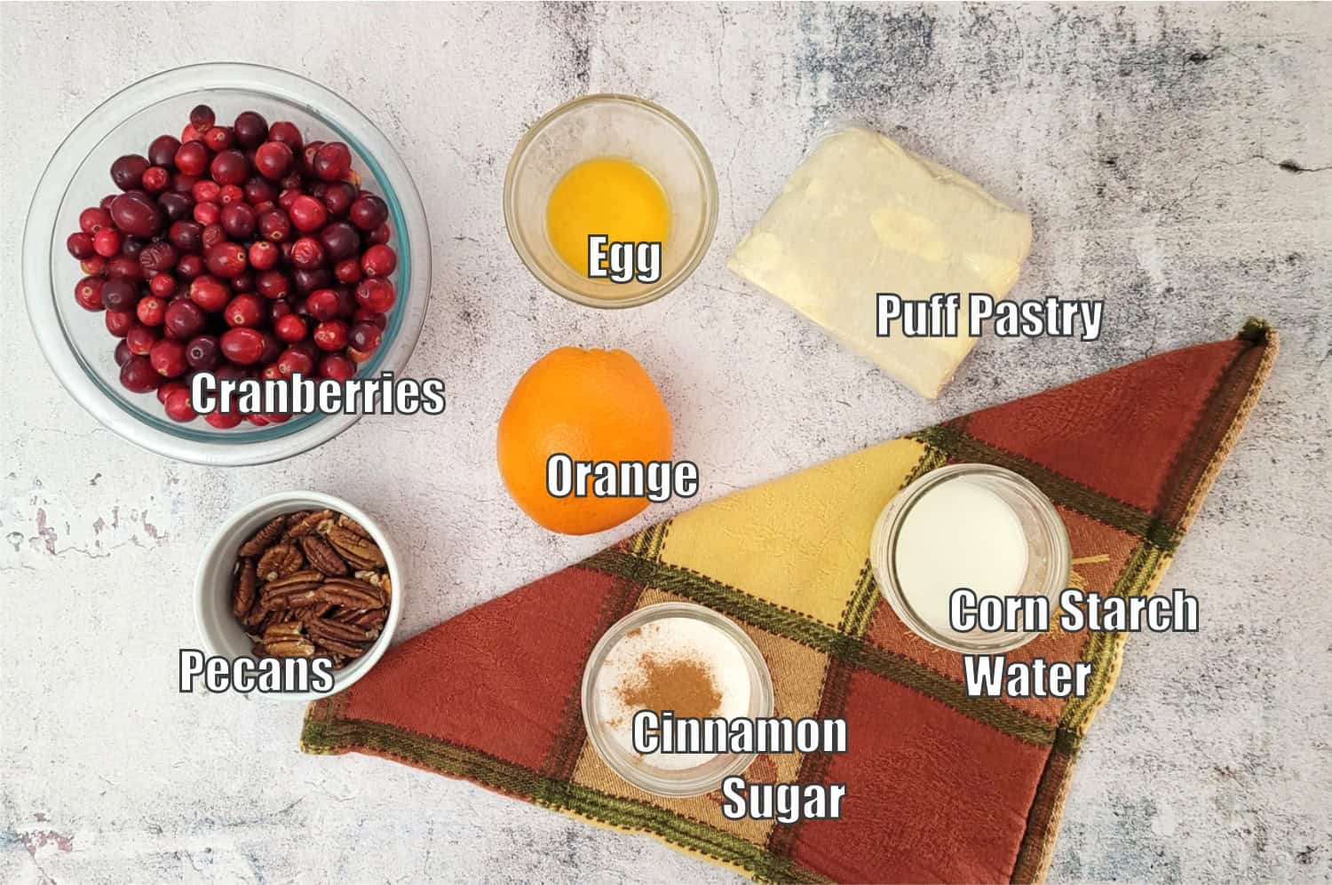 ingredients needed to make a cranberry galette recipe including puff pastry, cornstarch, water, cinnamon, sugar, orange, pecans, egg and fresh cranberries