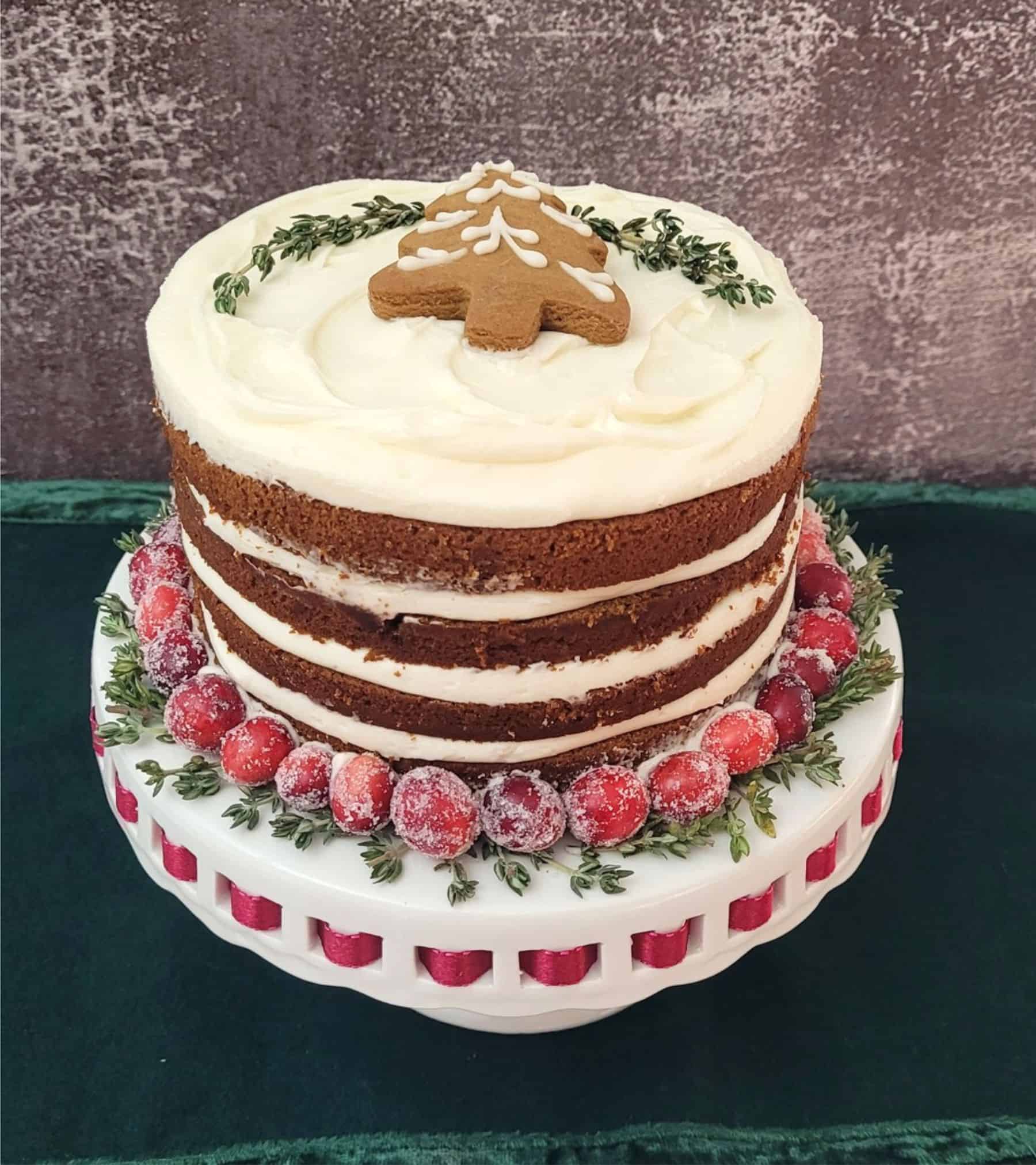 finished cake on a cake stand and decorated with a gingerbread cookie and candied cranberries