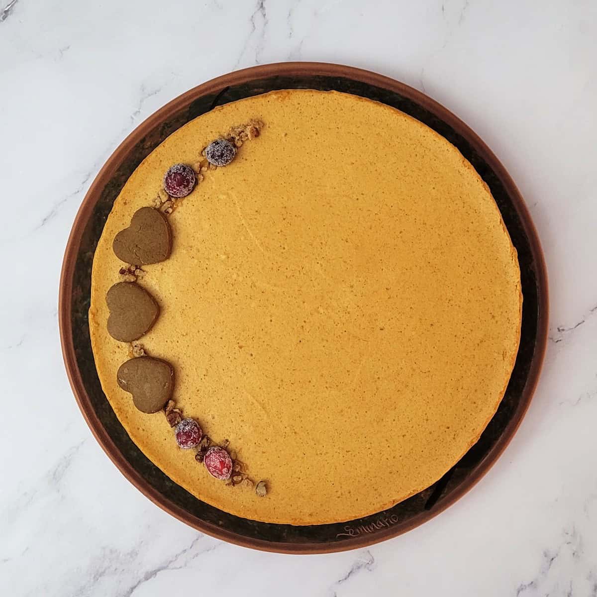 overhead view of pumpkin mousse cake decorated with gingerbread heart cookies, candied cranberries and pecan pieces