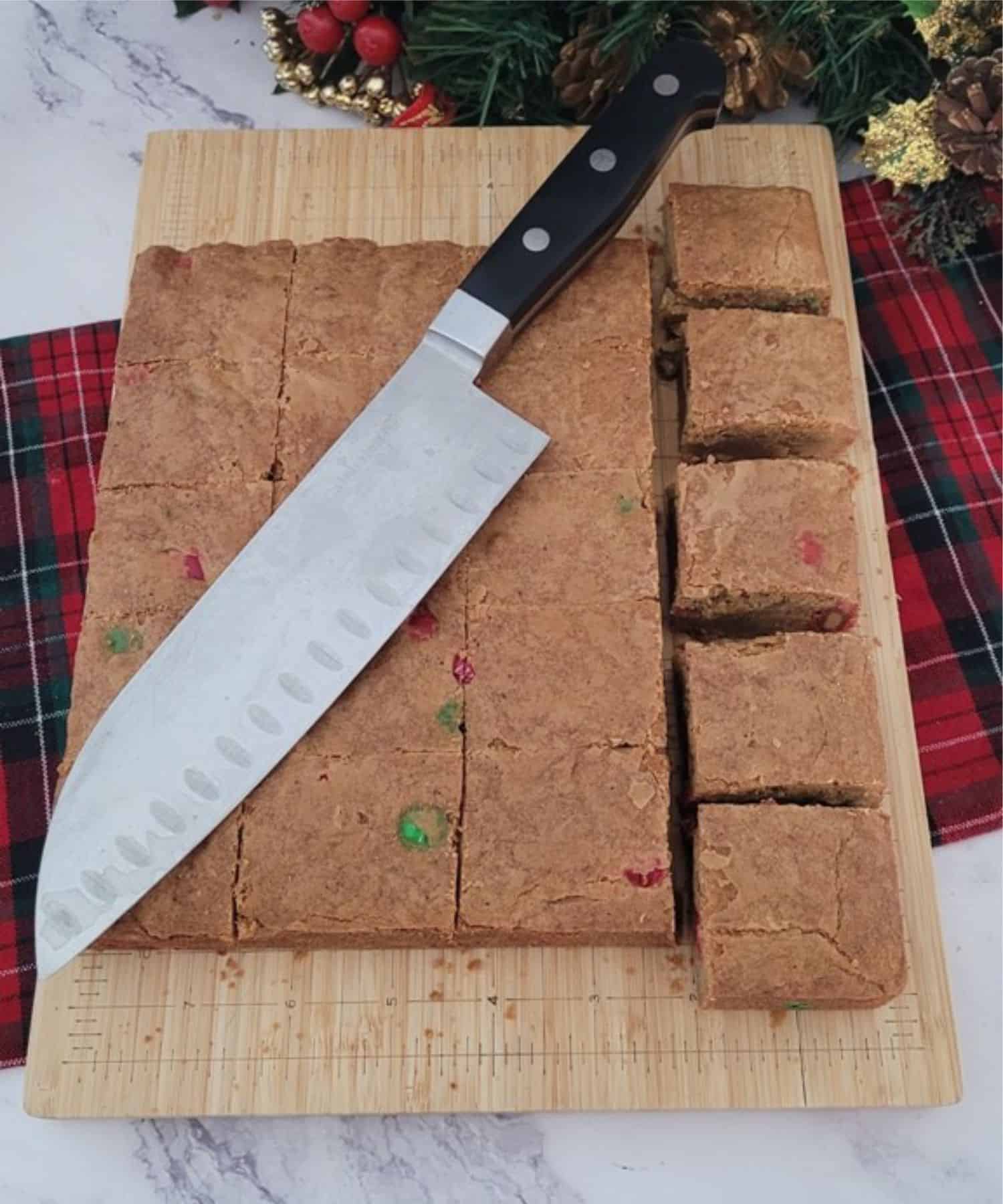 cutting board with holiday brown butter blondies being sliced into 20 pieces