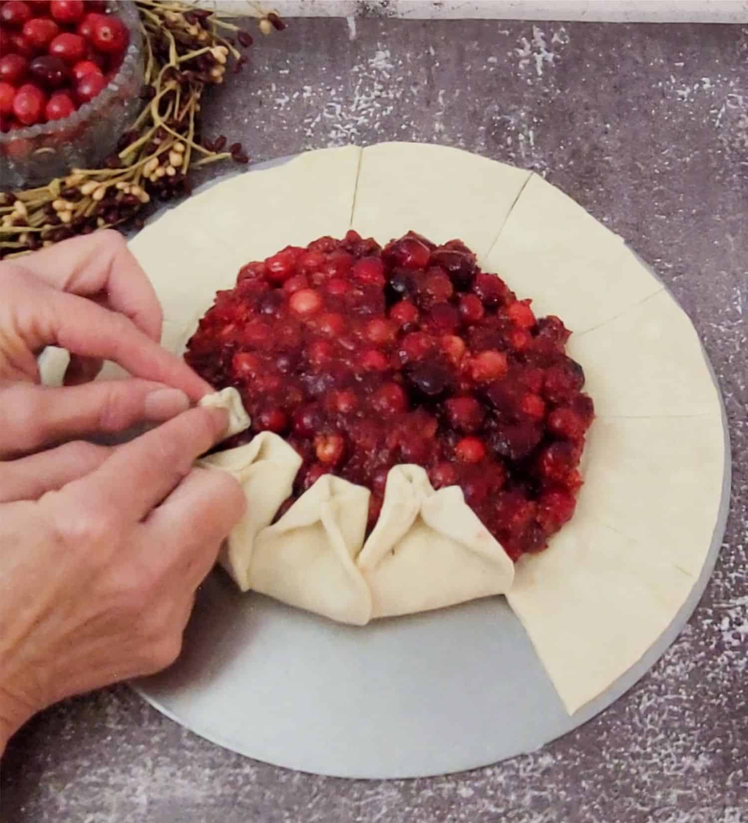 folding edges of puff pastry over to make decorative edge for cranberry galette with orange