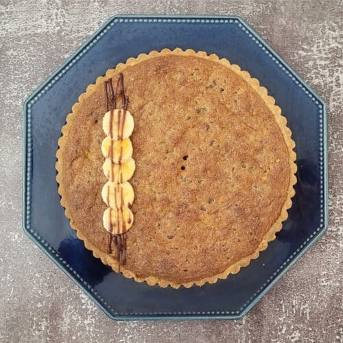 overhead view of a banana walnut tart with chocolate drizzle and a few brulee bananas