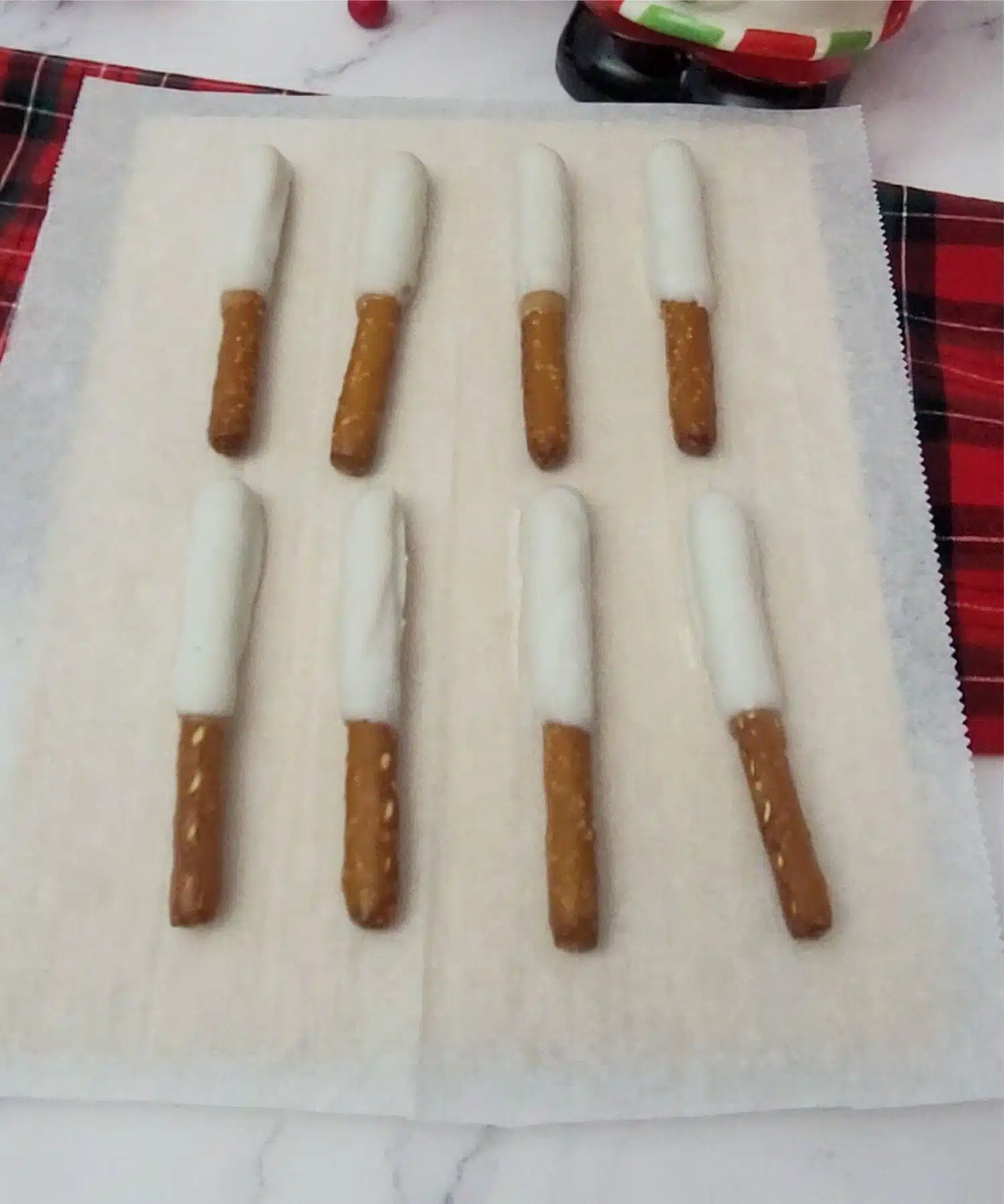 Christmas pretzel rods dipped in white chocolate and setting on parchment paper to dry