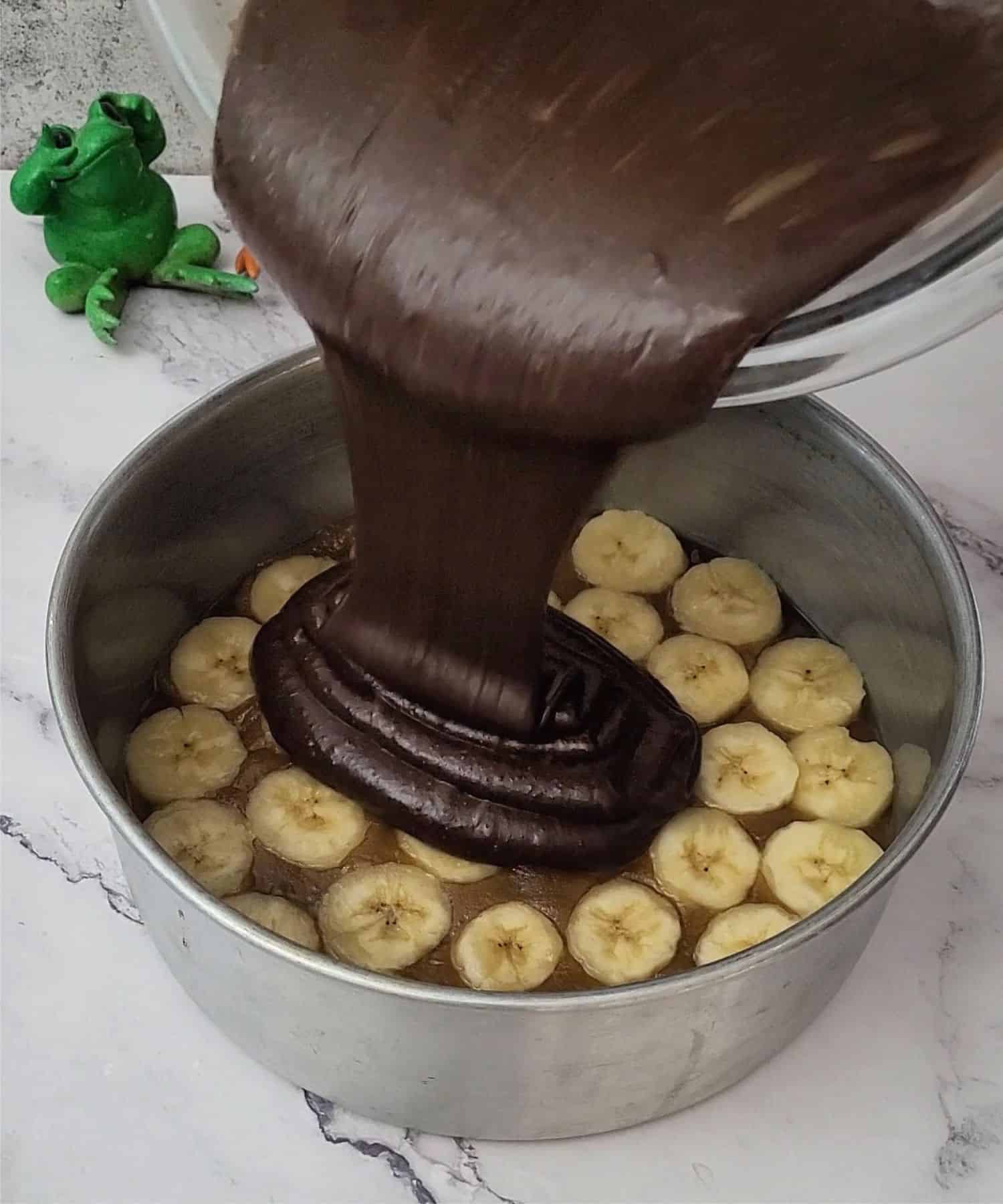 pouring chocolate cake batter over bananas and caramel topping