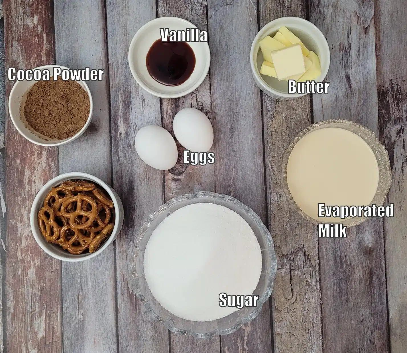 ingredients needed to make chocolate pretzel tart including cocoa powder, eggs, sugar, evaporated milk, butter and vanilla