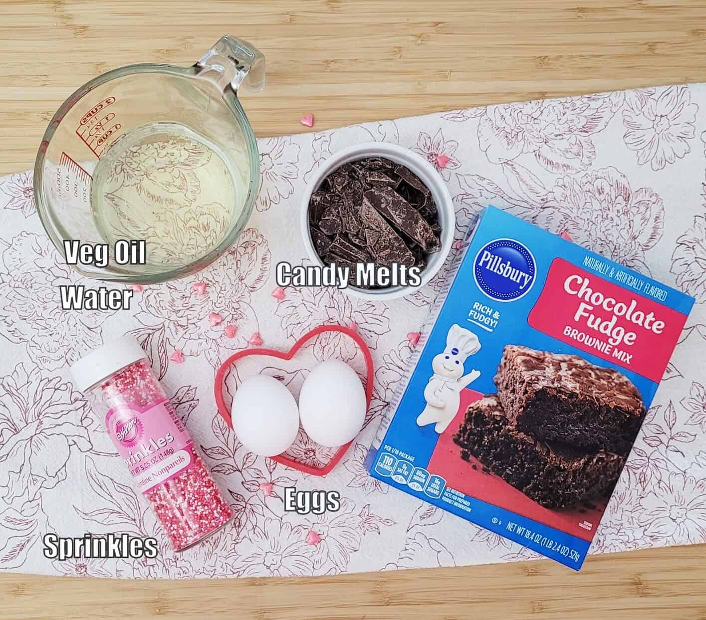 ingredients needed to make easy Valentine's day brownies including boxed brownie mix, eggs, vegetable oil, water, sprinkles and candy melts