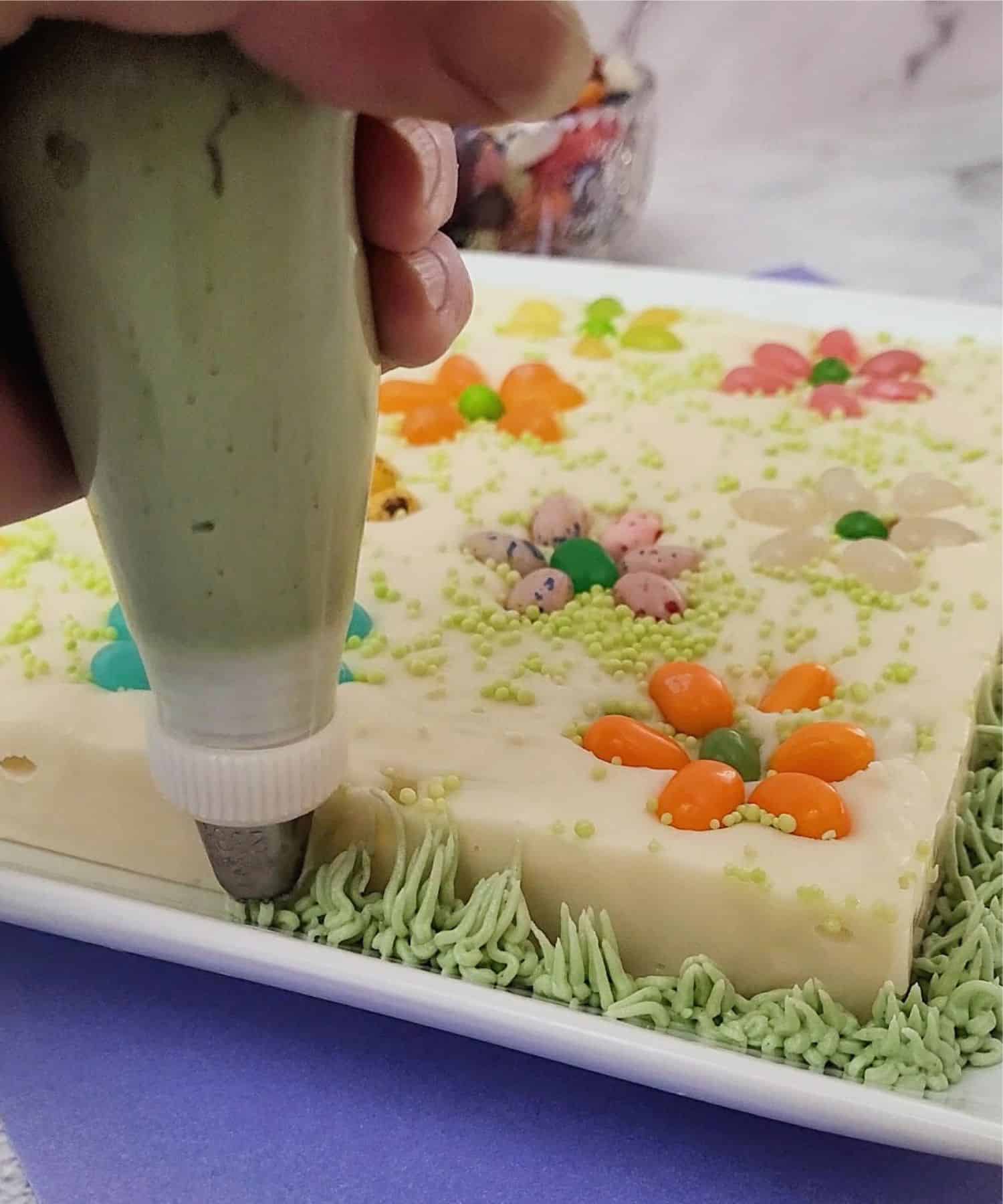 piping buttercream grass around fudge with jelly beans