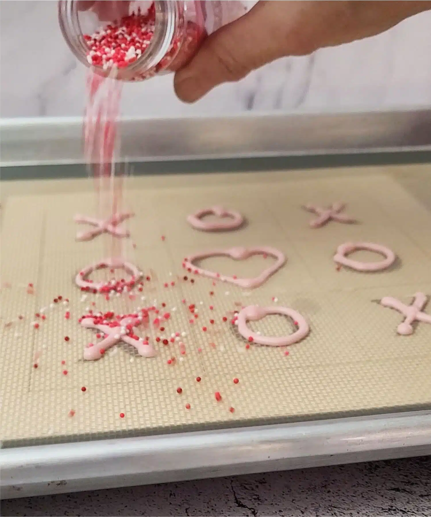 pouring pink, red and white sprinkles over chocolate decorations