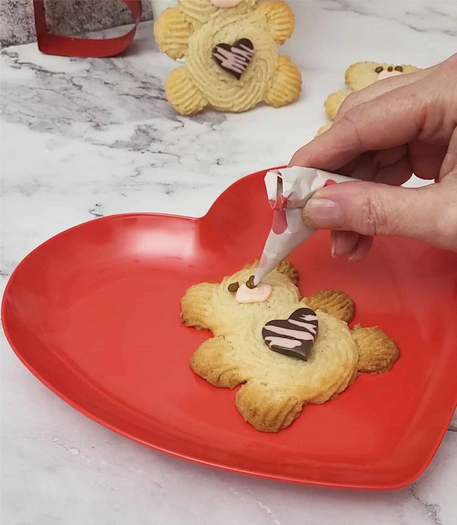 using royal icing to pipe snout, nose and eyes on Valentine Bear Cookies