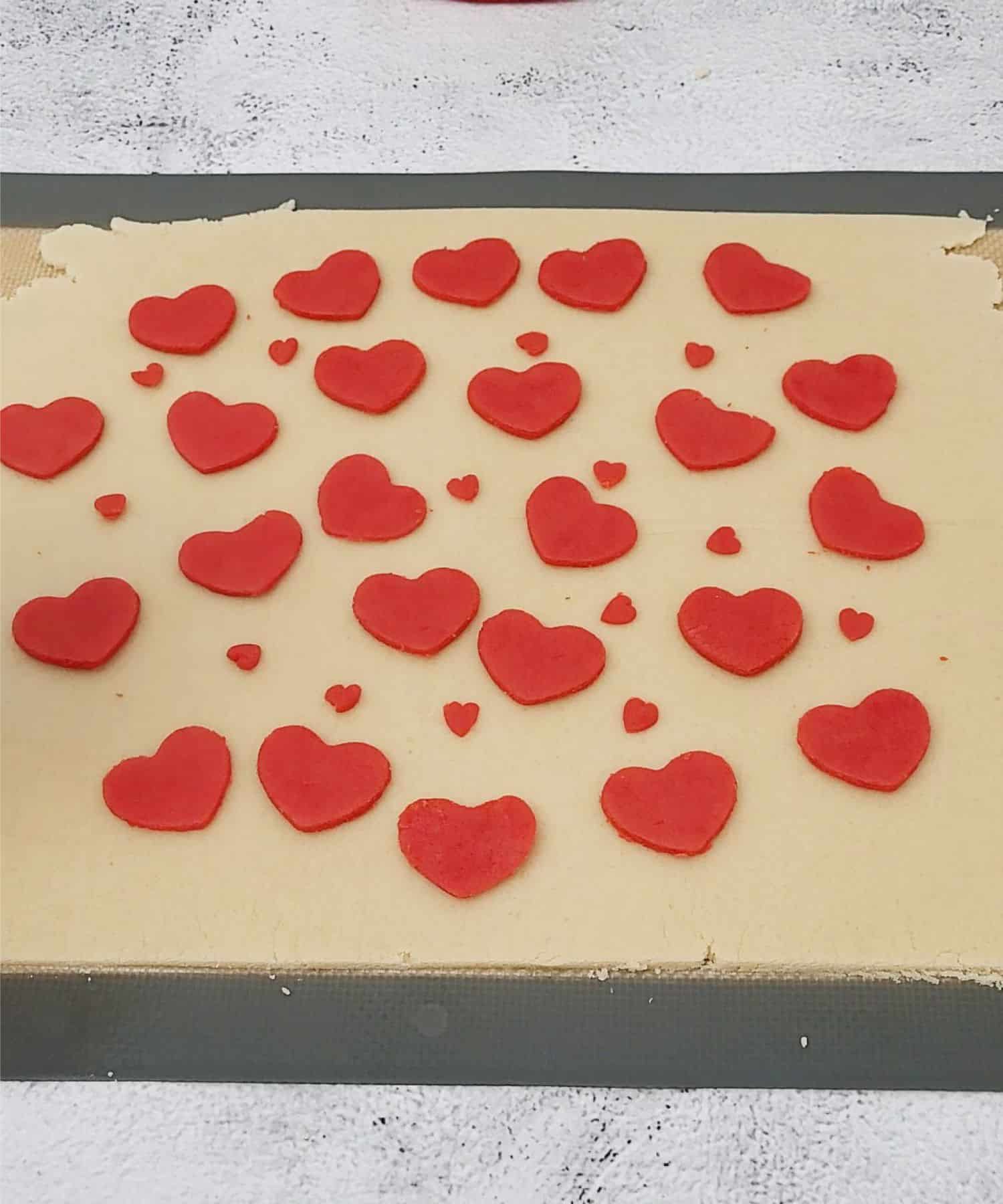 red hearts made from cookie dough placed over sheet of dough to start the inlay process