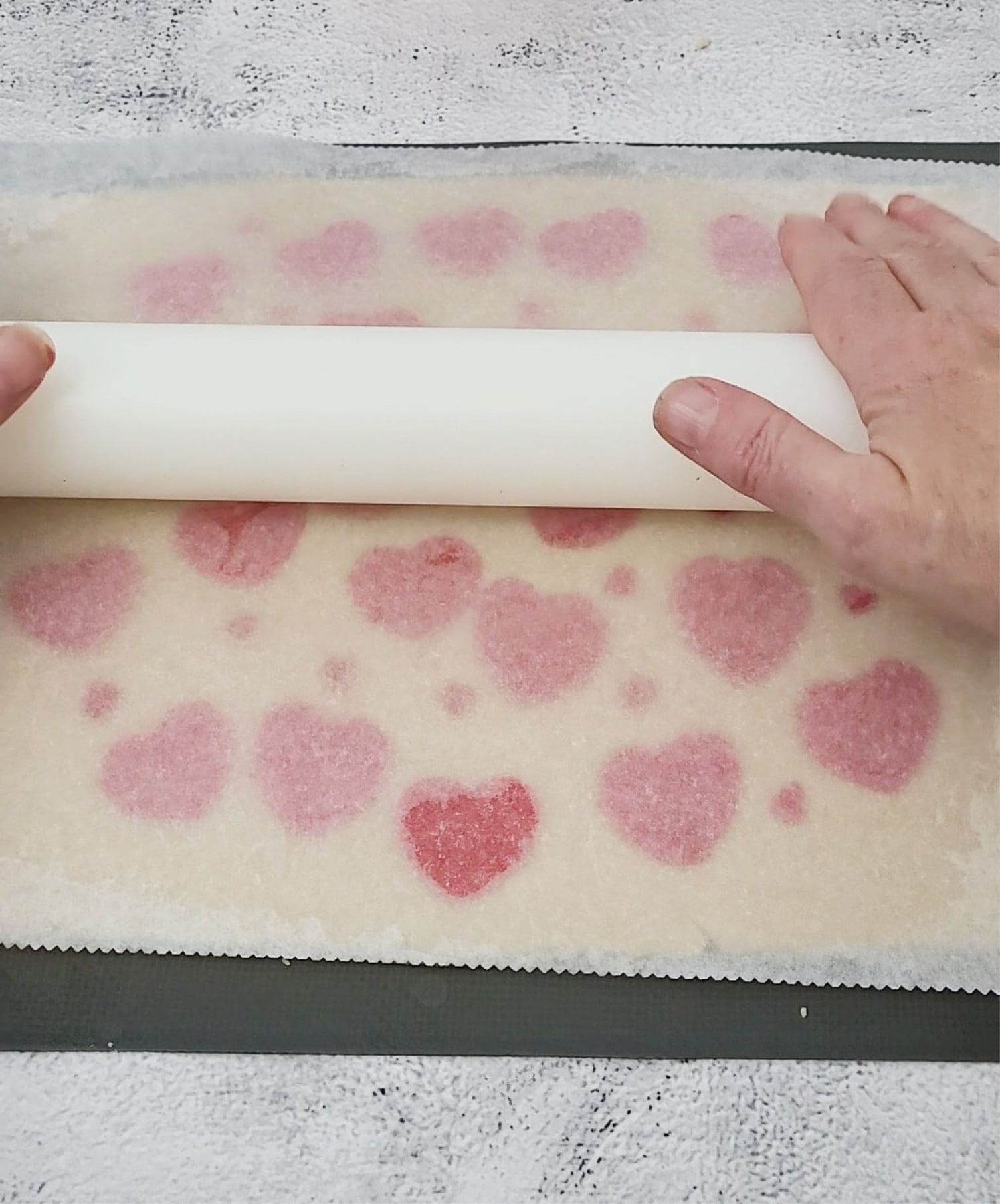 gently rolling a rolling pin over cookie dough to adhere red hearts before baking