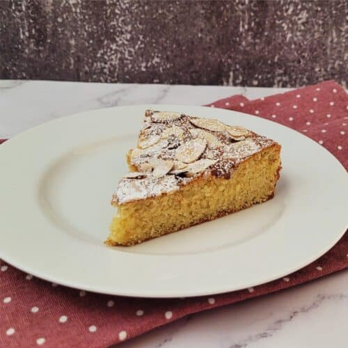 slice of almond flour cake on a plate with powdered sugar sprinkled over the top