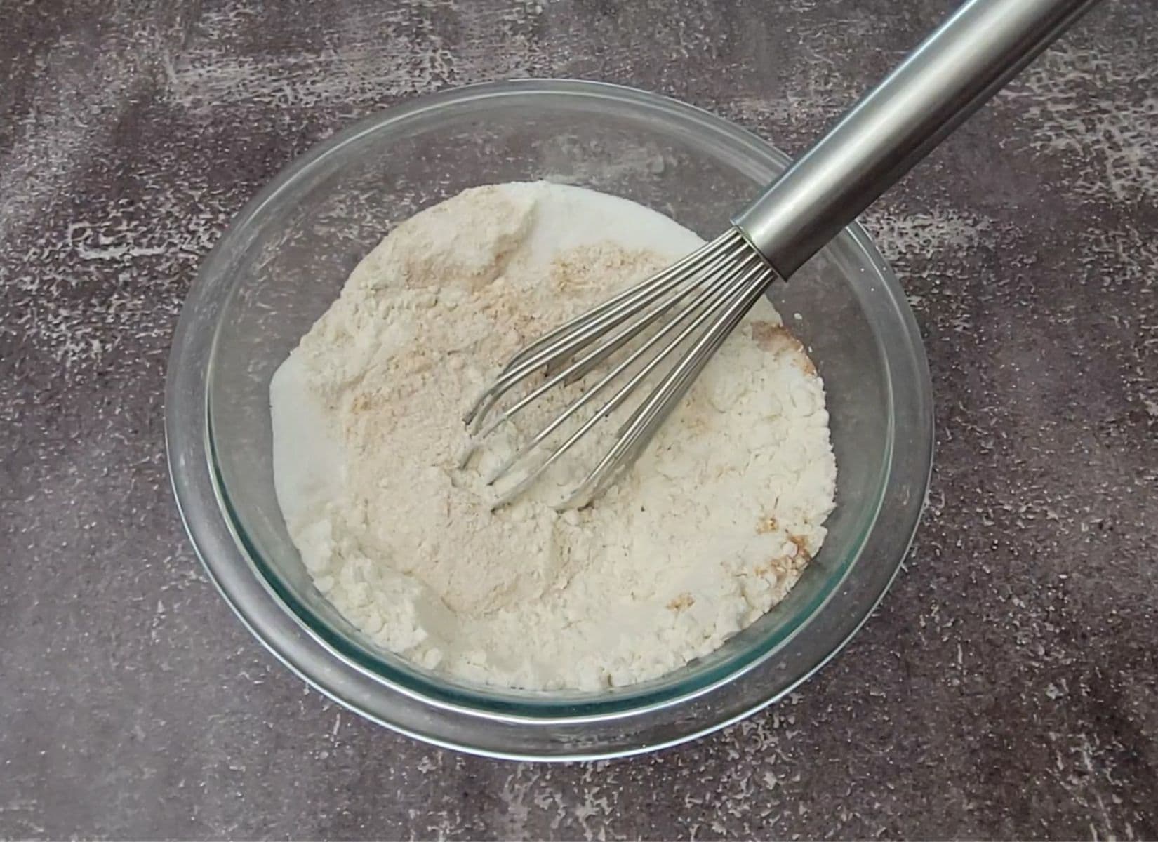 combining dry ingredients including flour, sugar, baking powder, salt, baking soda and cinnamon in a mixing bowl