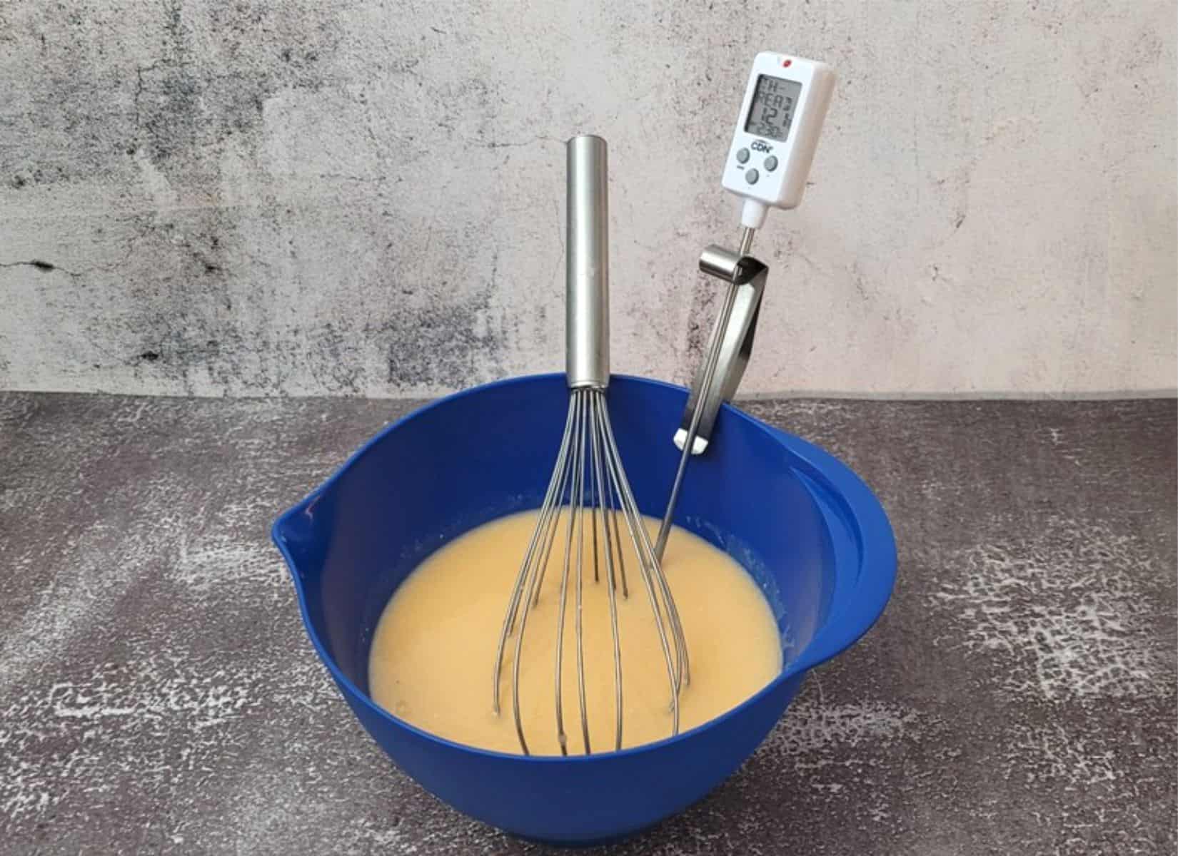 mirror glaze in a bowl with a thermometer to track glaze cooling to 90 degrees