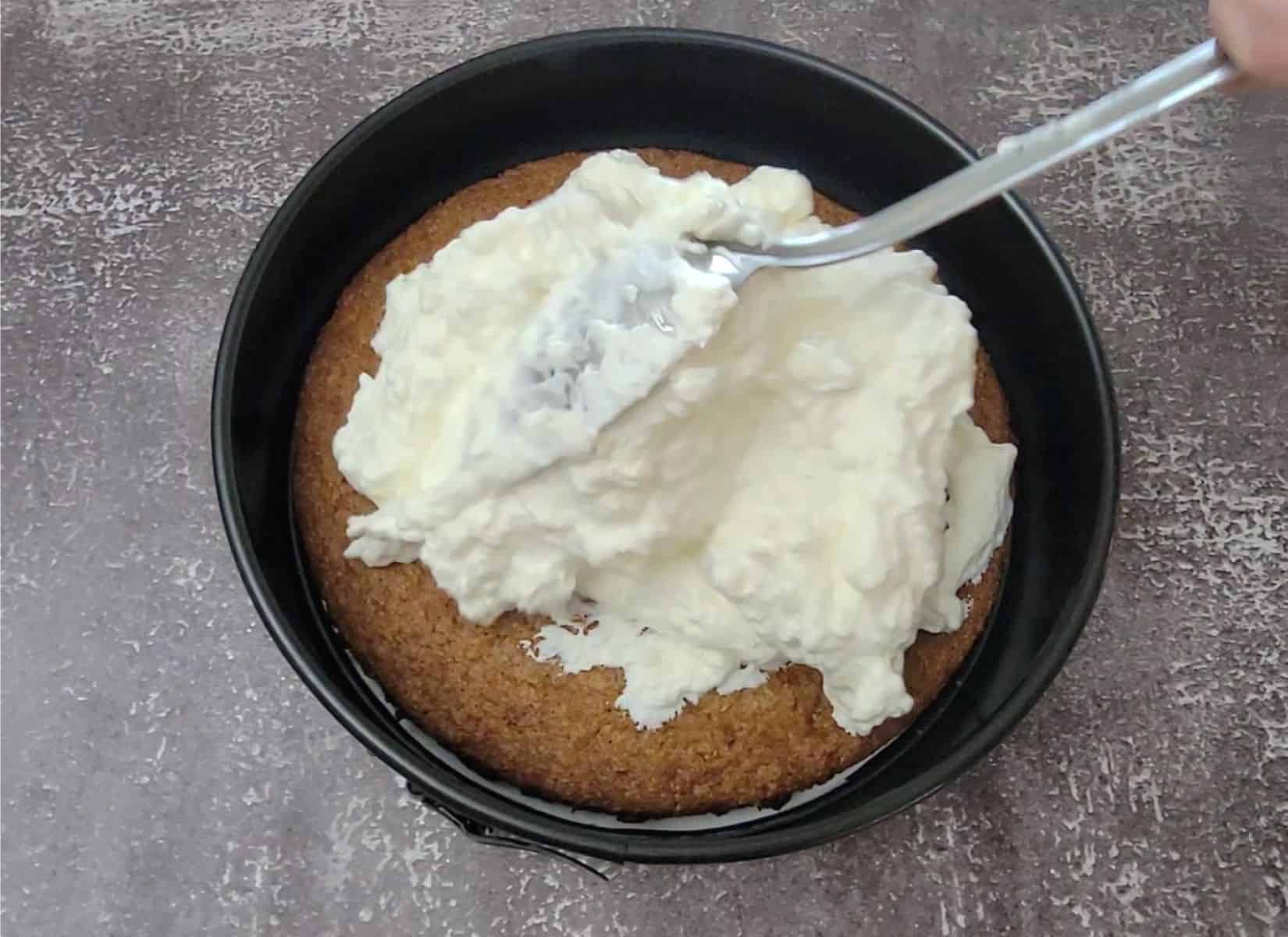 scooping cream cheese mousse over top of eggless carrot cake in a springform pan