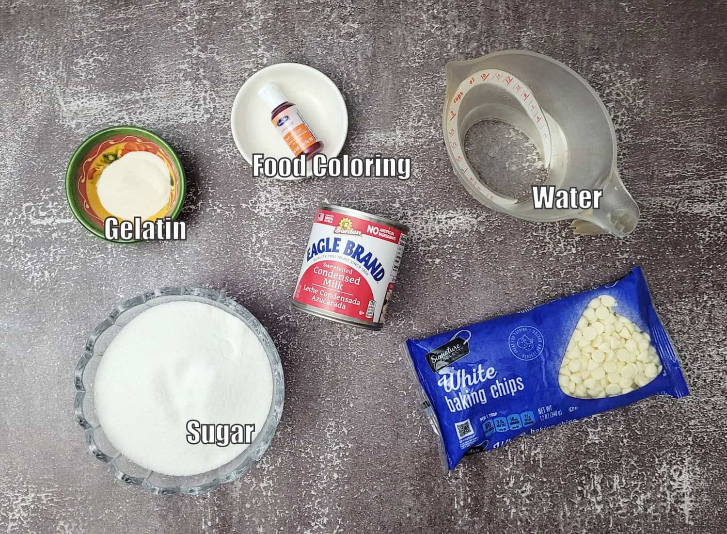 ingredients needed to make mirror glaze including food coloring, gelatin, water, granulated sugar, sweetened condensed milk and white chocolate chips