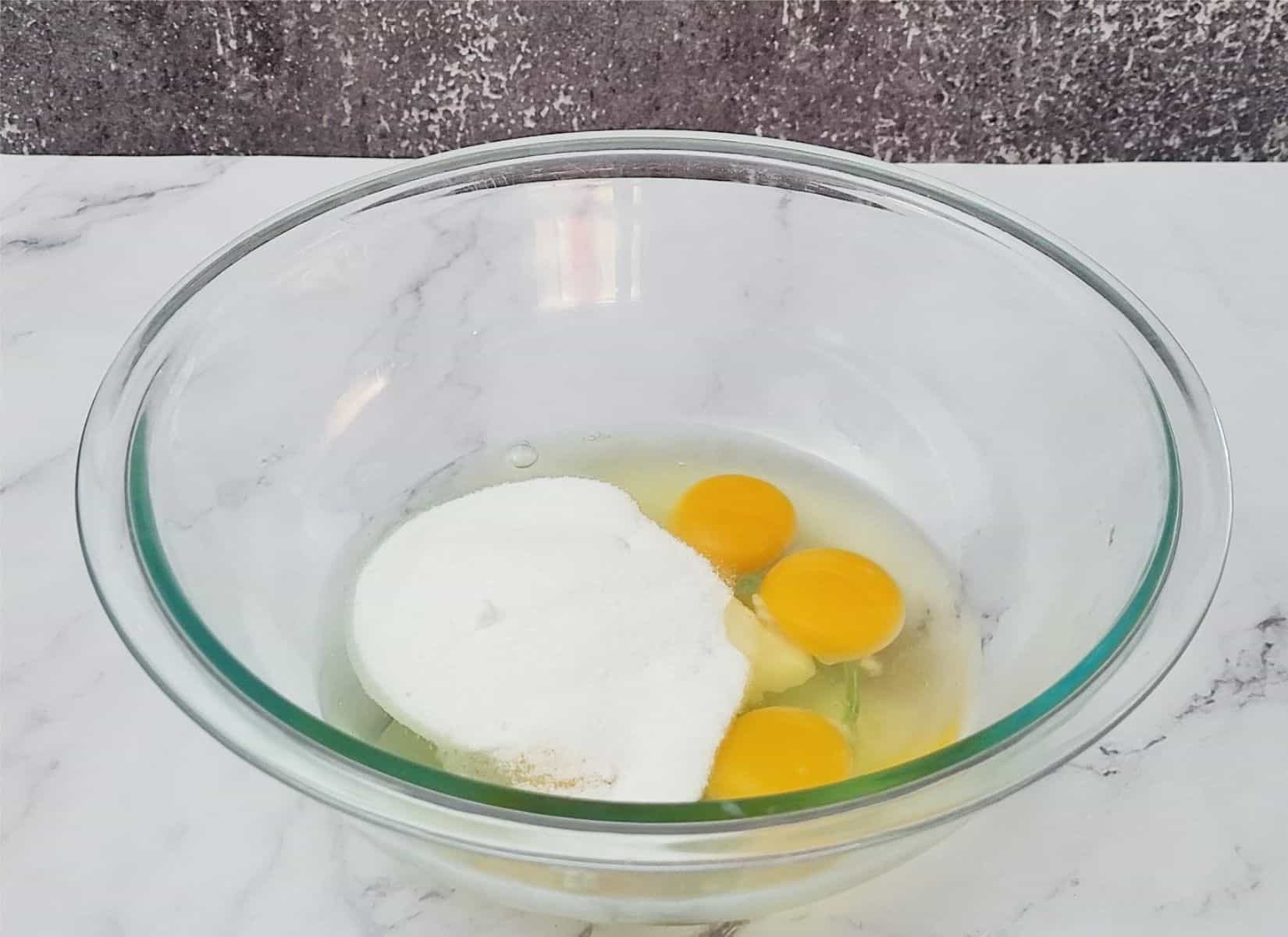 granulated sugar and four eggs in a glass mixing bowl