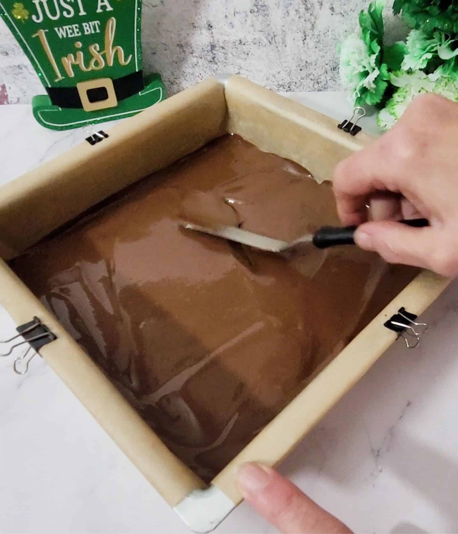 using an offset spatula to spread melted chocolate in pan to make candy