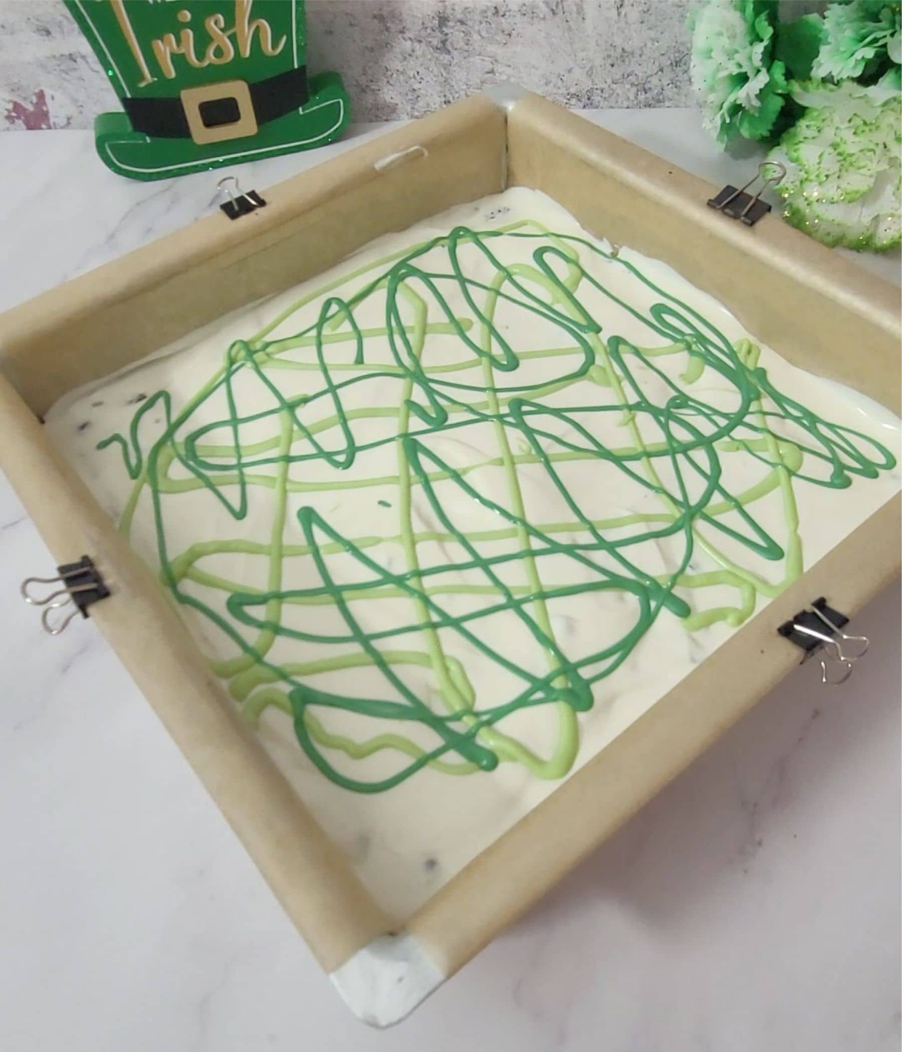 varying shades of green candy melts drizzled into pan to make Oreo bark for St. Patrick's Day