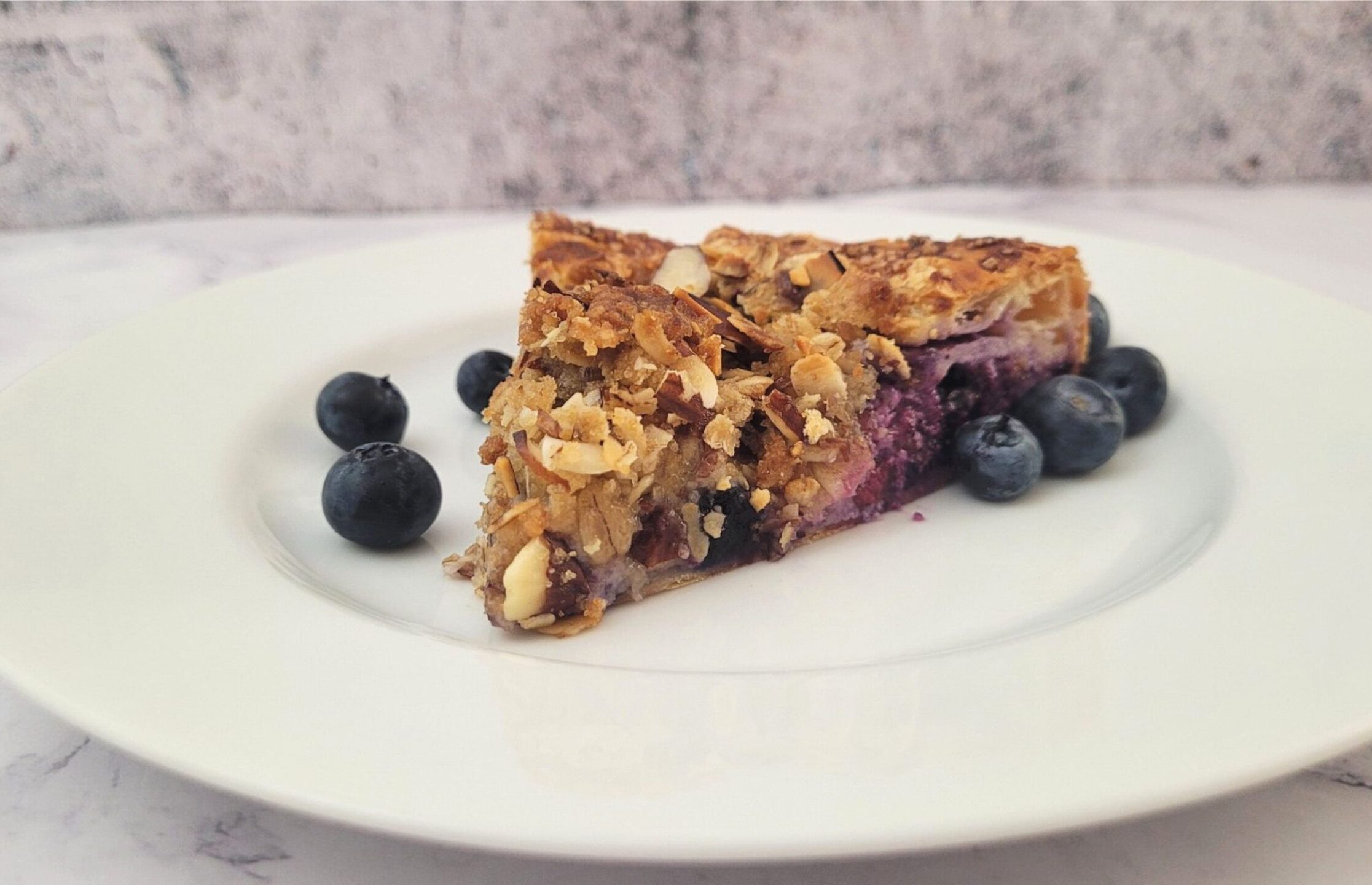 slice of rustic blueberry almond galette on a plate and a few blueberries scattered on plate