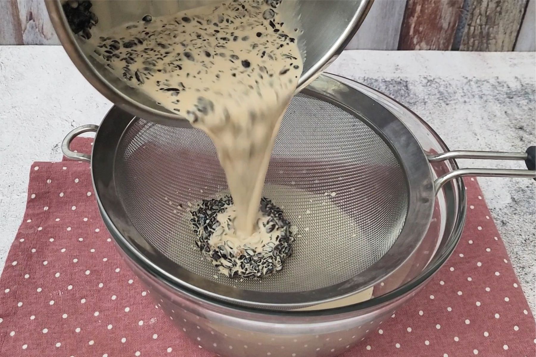 straining custard through mesh sieve to remove coffee bean pieces
