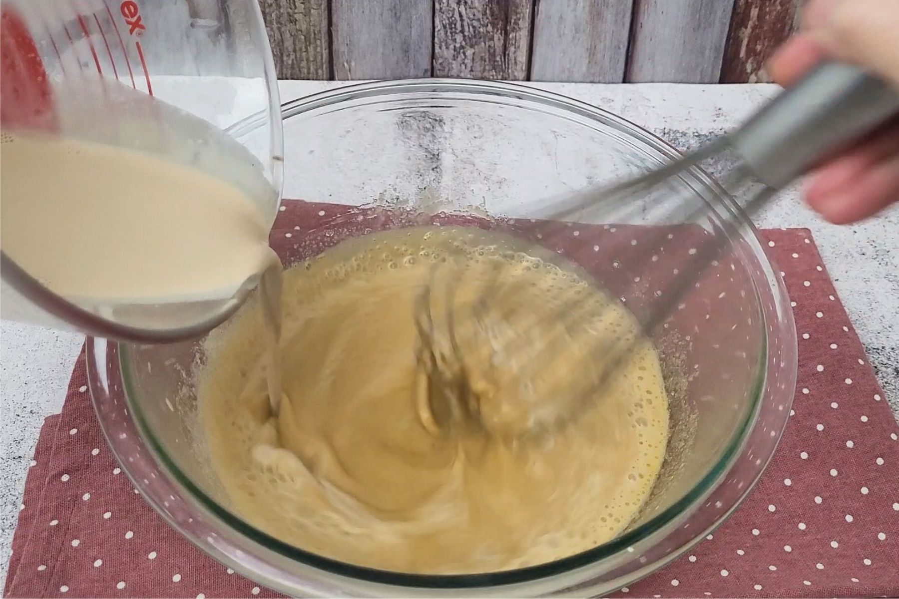 slowly pouring hot cream into eggs while whisking to temper egg yolks