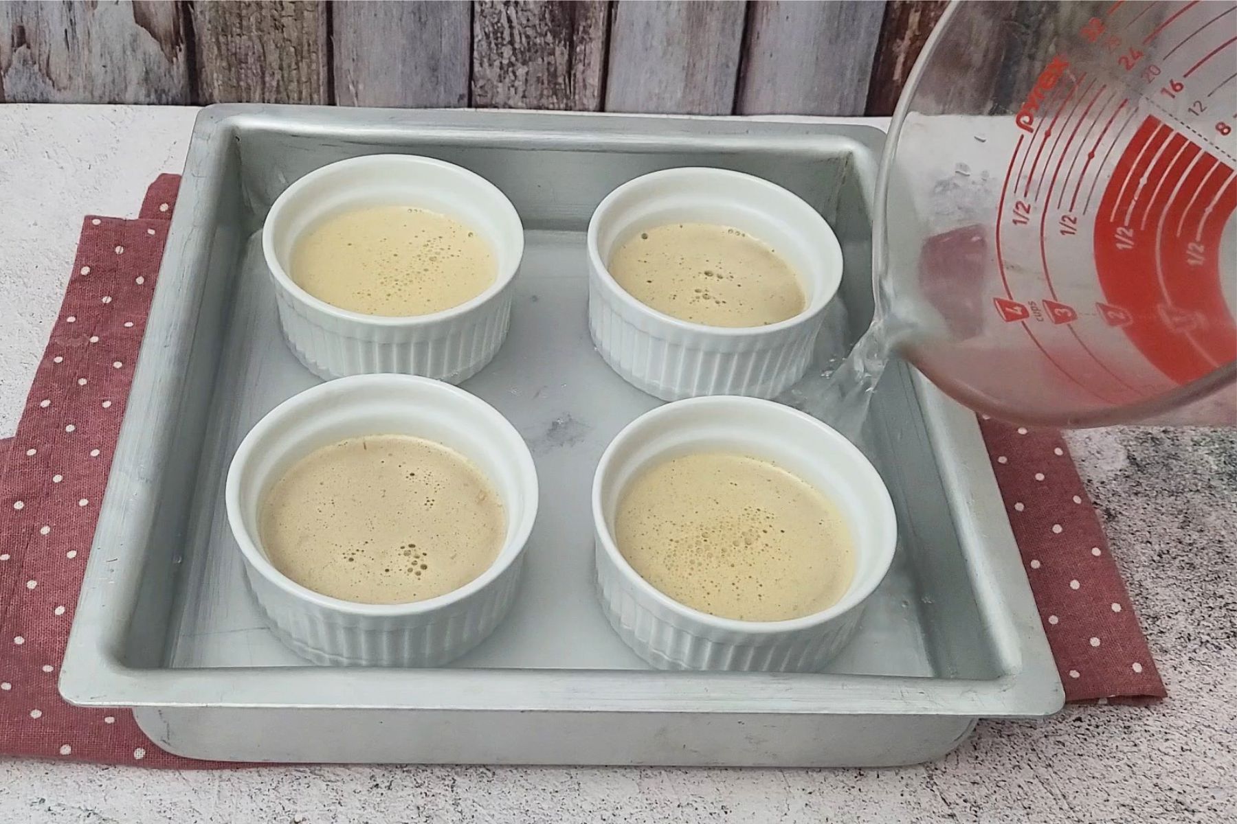 pouring water into baking pan so it reaches halfway up ramekins to evenly bake coffee crème brulee