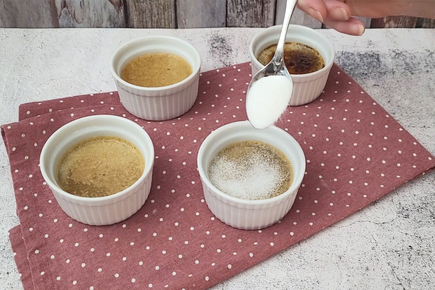four coffee crème brulee ramekins on napkin with one being sprinkled with granulated sugar