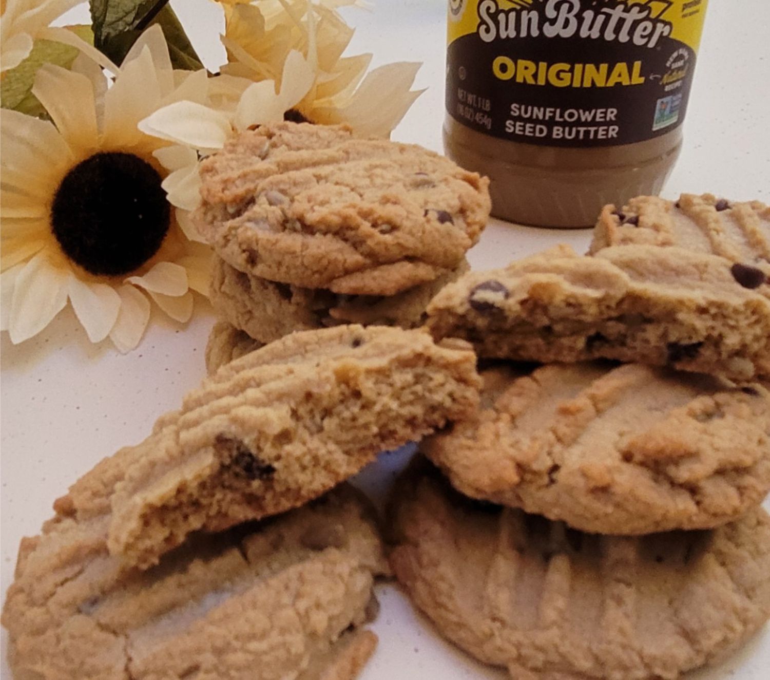 cookies made with sunbutter on a countertop with a jar of sunbutter and sunflowers in the background