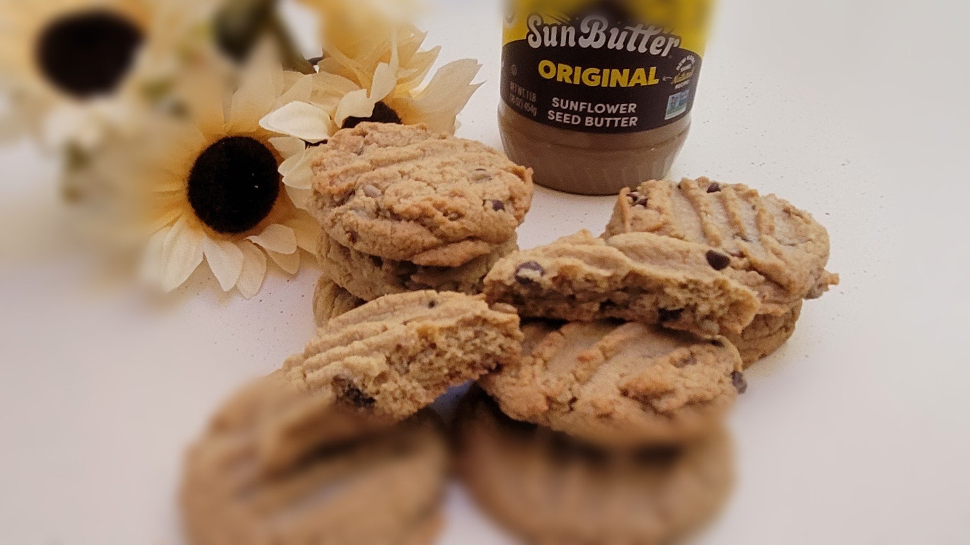 finished sunbutter cookies on a countertop with a jar of sunbutter and sunflowers in the background