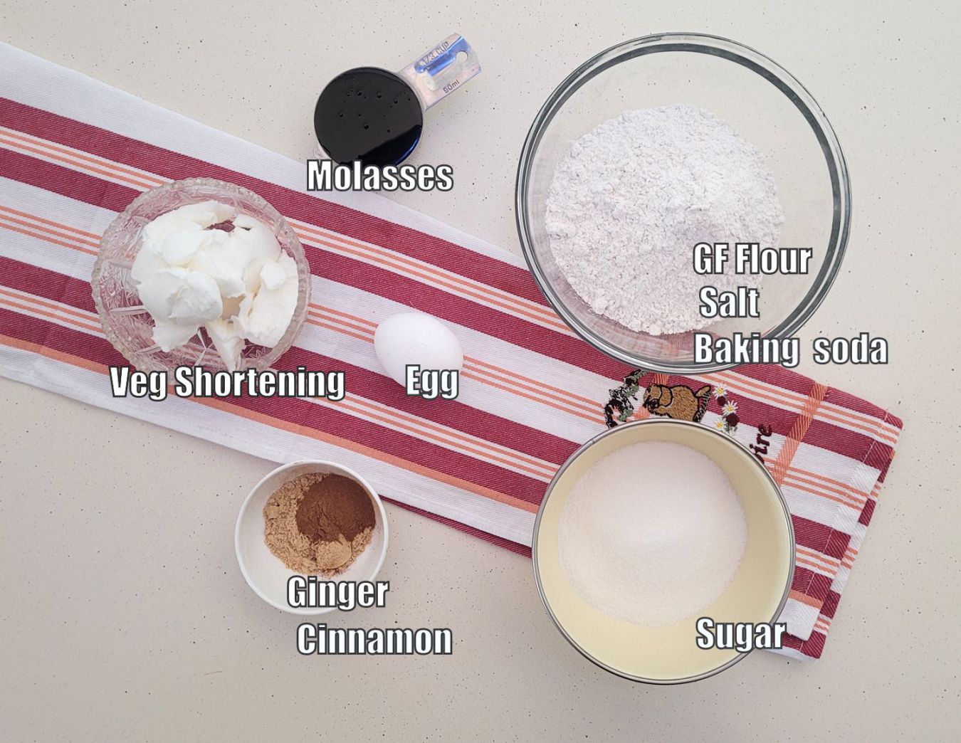 ingredients needed to make cookie recipe including granulated sugar, ginger, cinnamon, an egg, vegetable shortening, gluten free flour, salt, molasses and baking soda