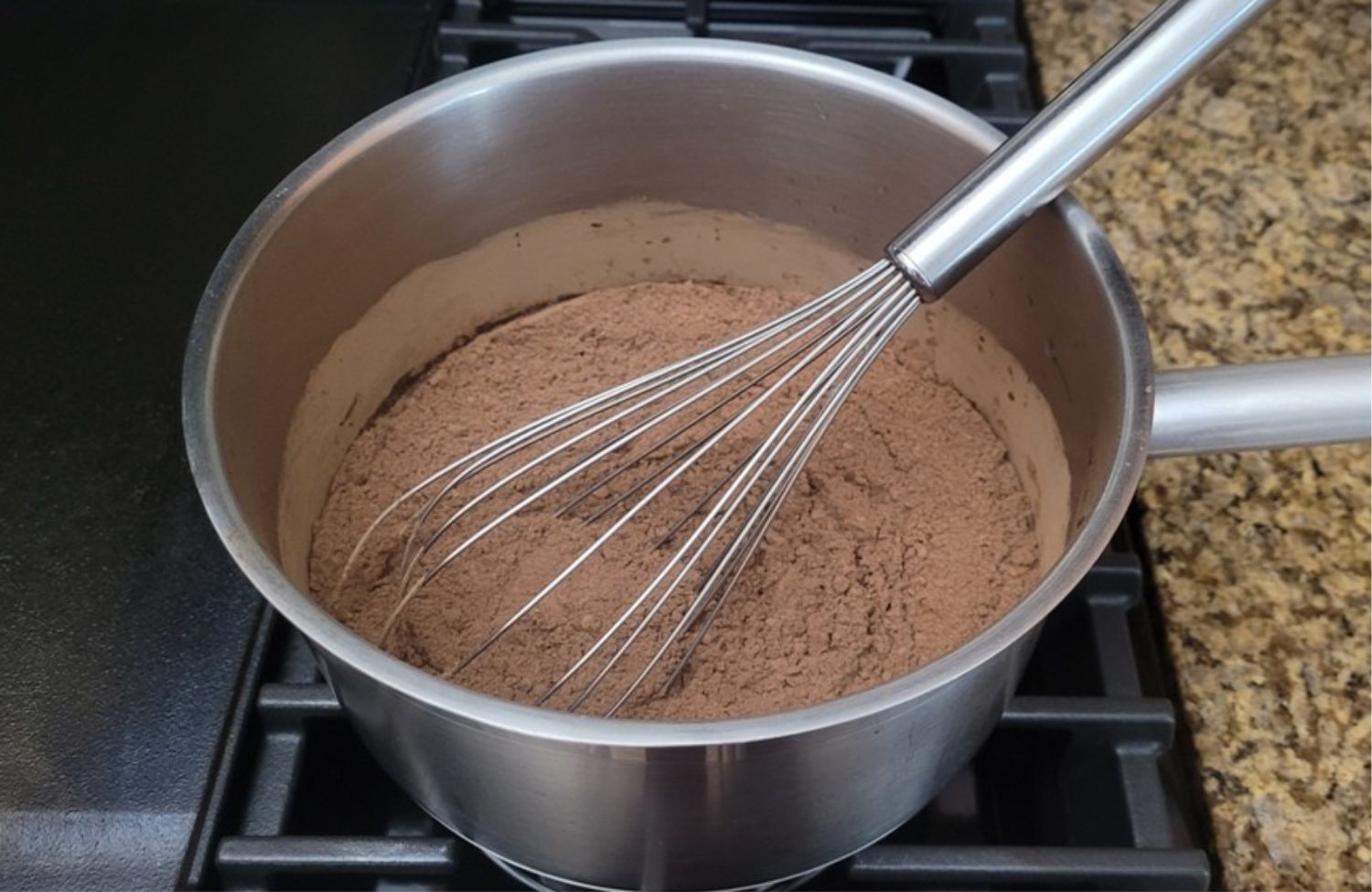 whisk and saucepan over stove with ingredients to make chocolate sauce